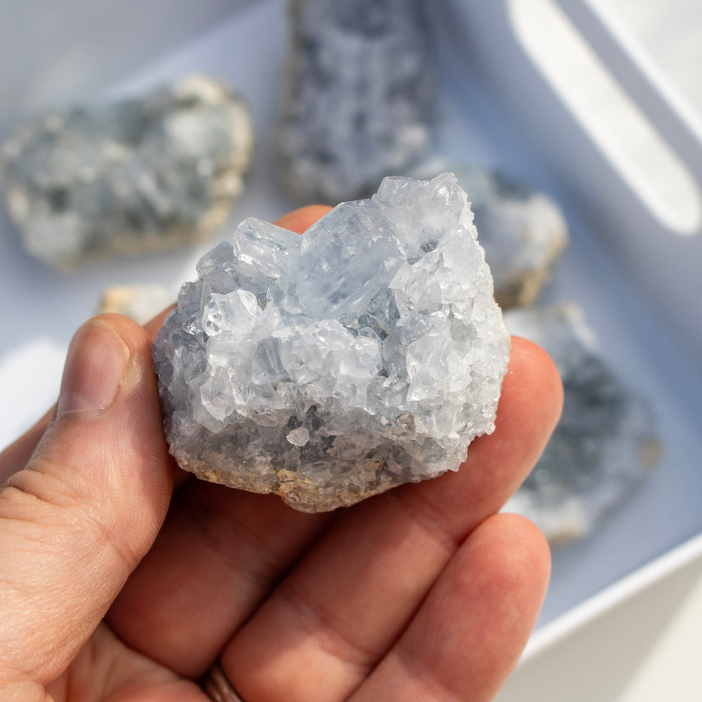 Hand holding a crystal rock with more crystals in the background