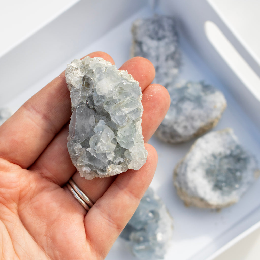 Hand holding a crystal rock with more crystals in the background on a white tray