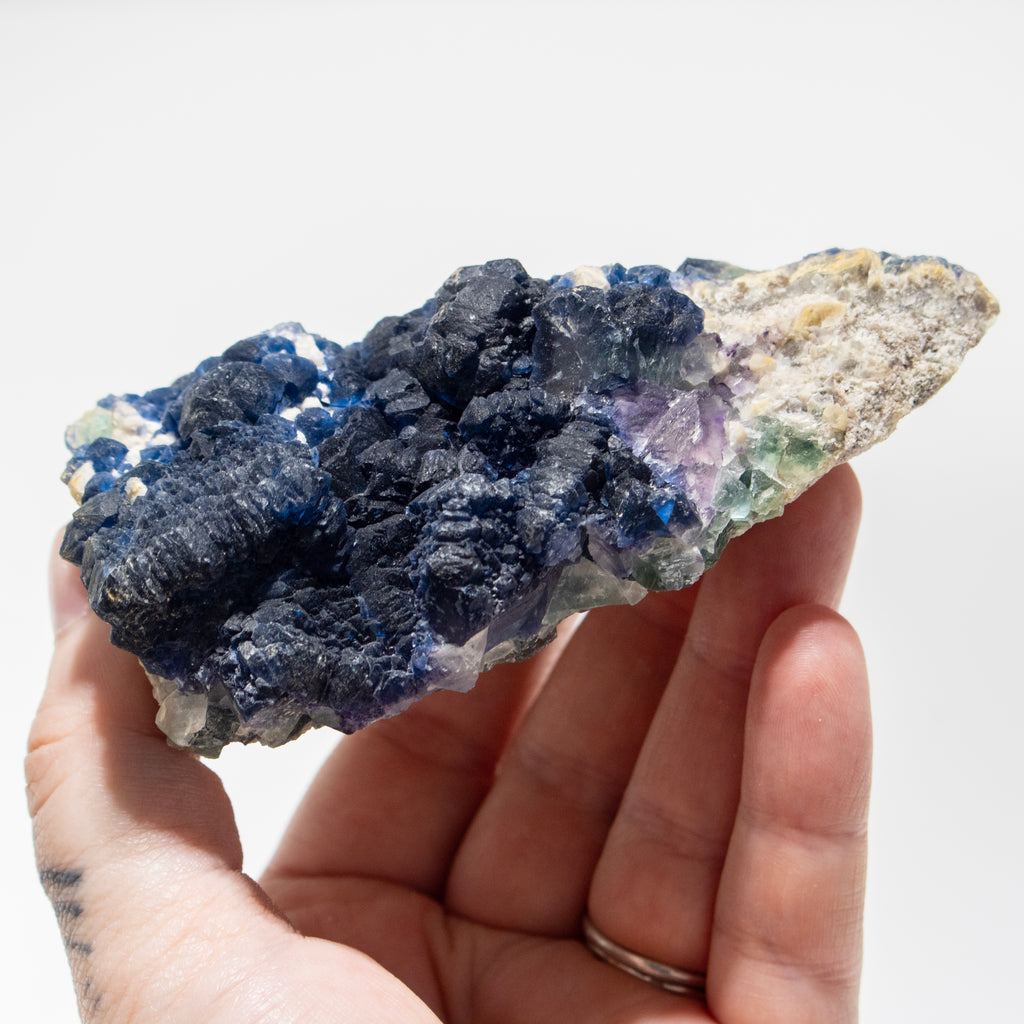 Hand holding a crystal rock with blue and purple minerals on a white background