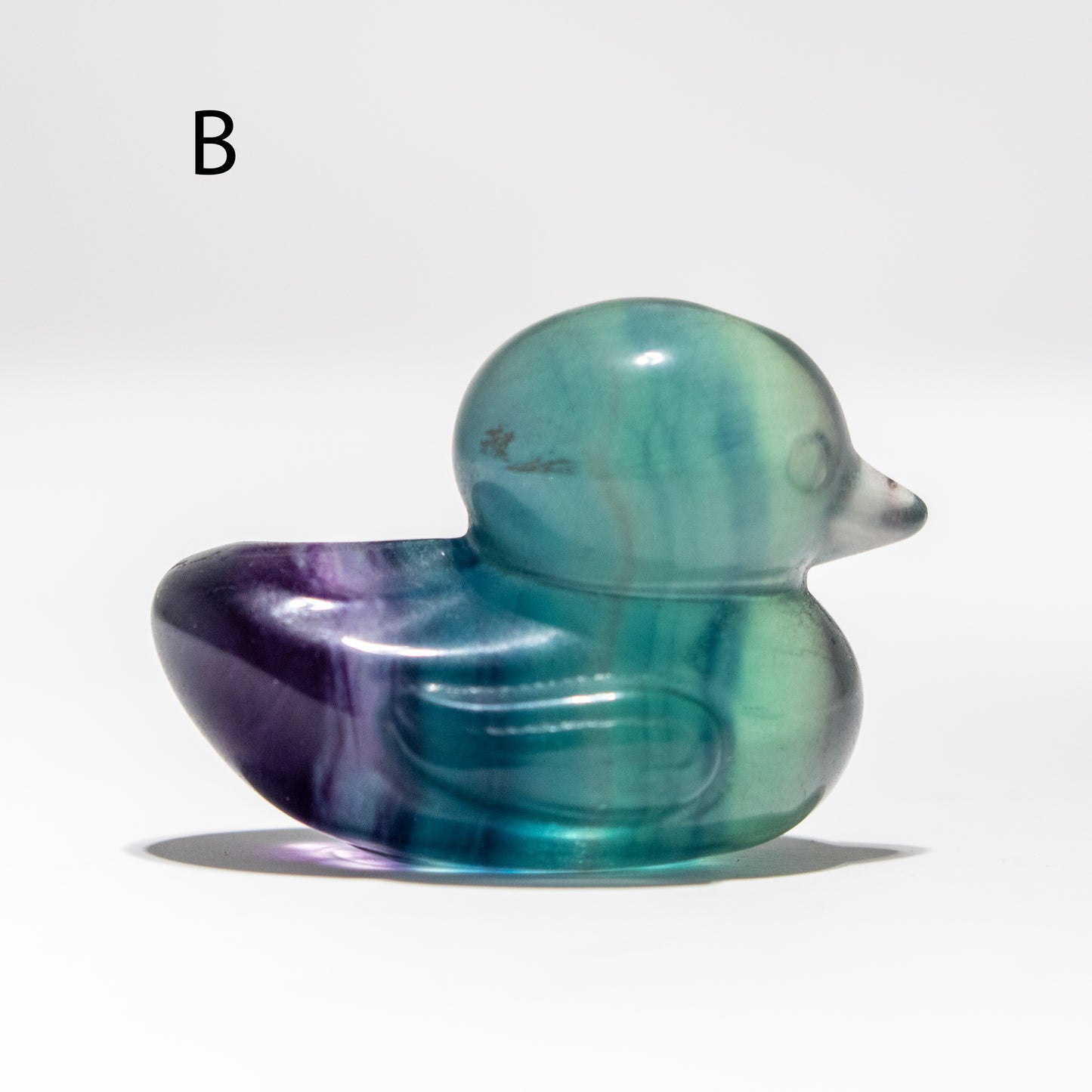Marbled purple and green duck-shaped crystal on a white background
