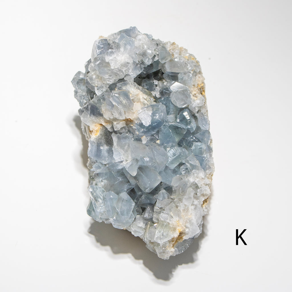 Crystal cluster on a white background with a letter 'K' in the corner