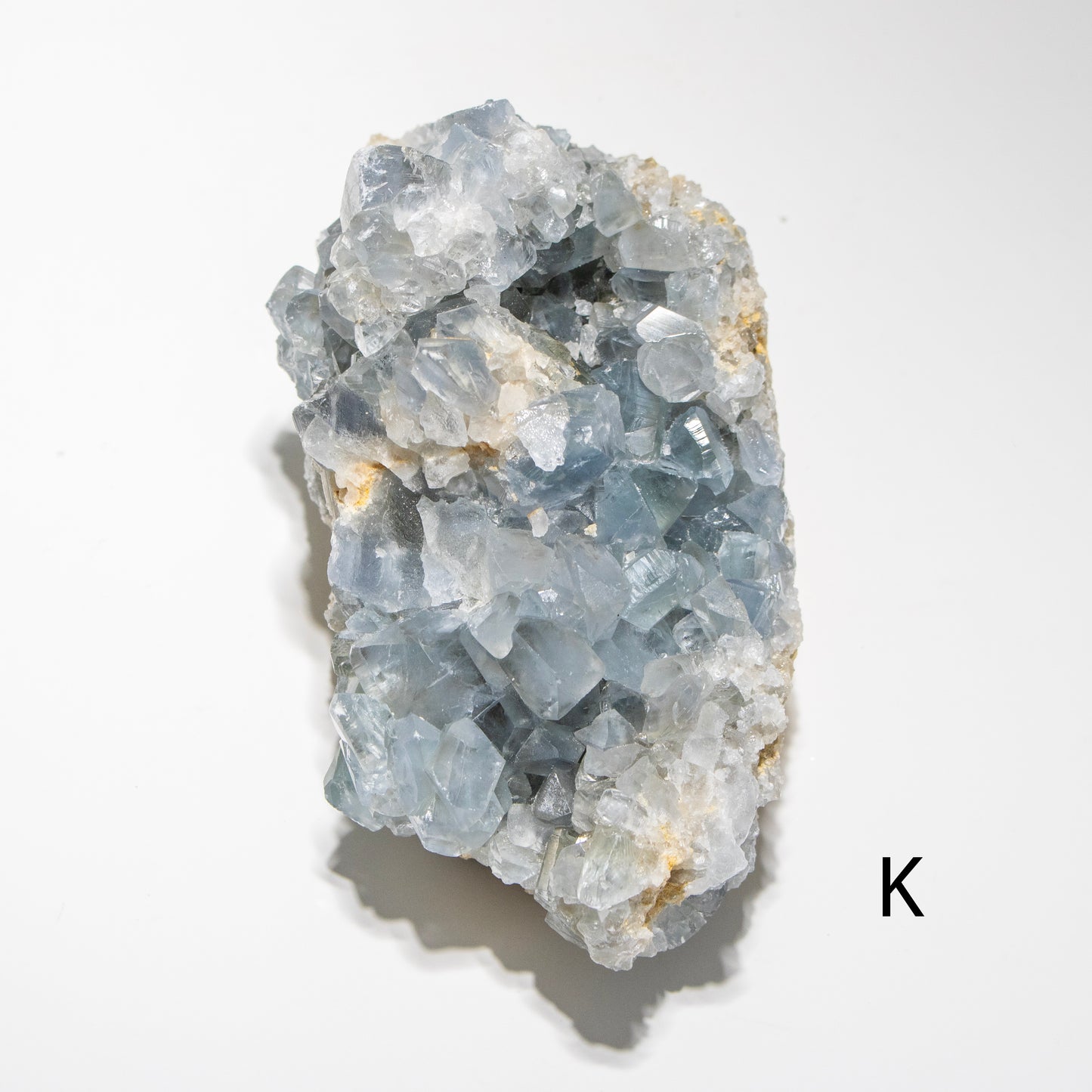 Crystal cluster on a white background with a letter 'K' in the corner