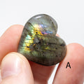 Heart-shaped labradorite stone held between fingers on a white background
