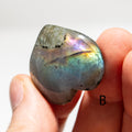 Multicolored labradorite stone held between fingers against a white background