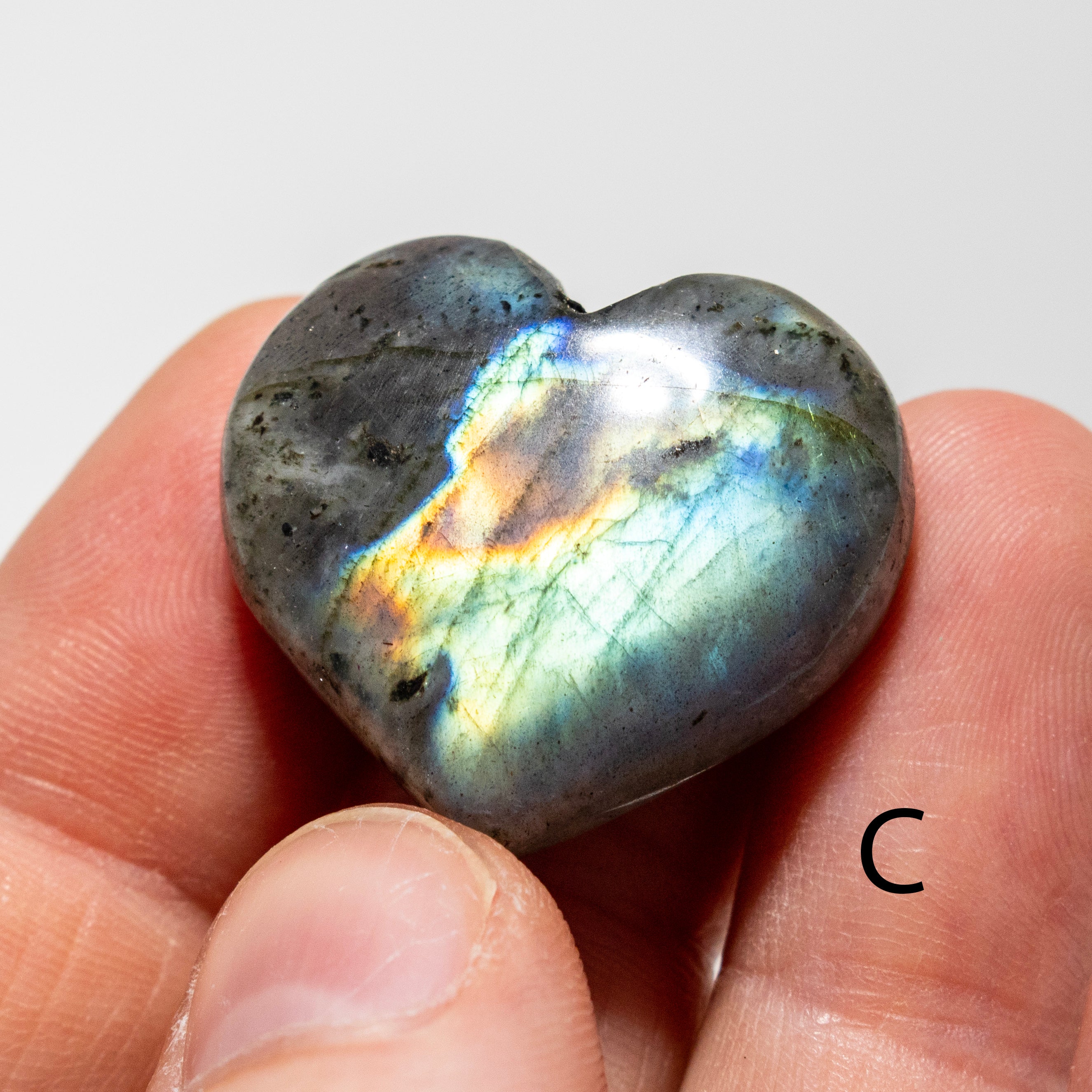 Heart-shaped labradorite stone held between fingers on a light background