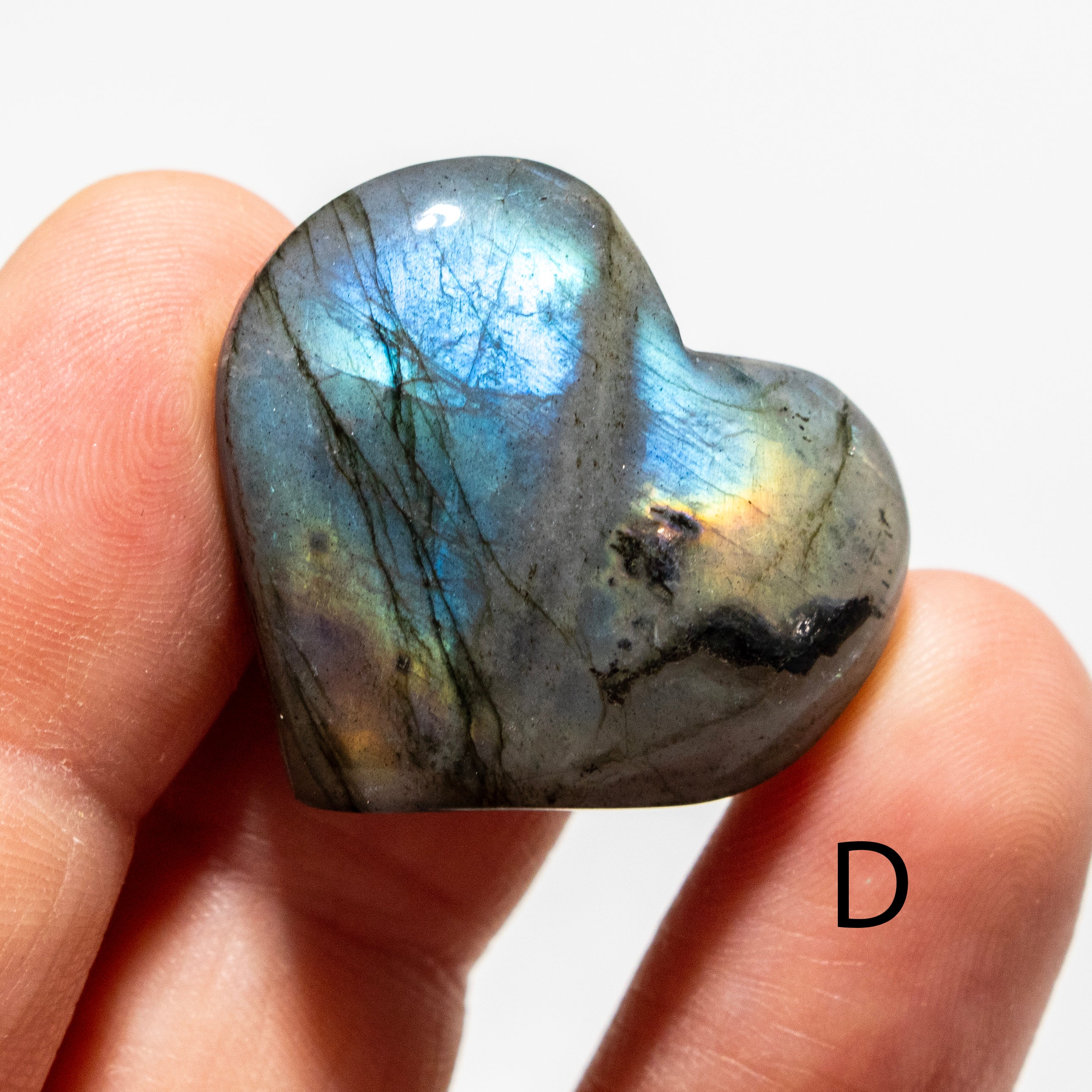 Heart-shaped labradorite stone held between fingers on a white background