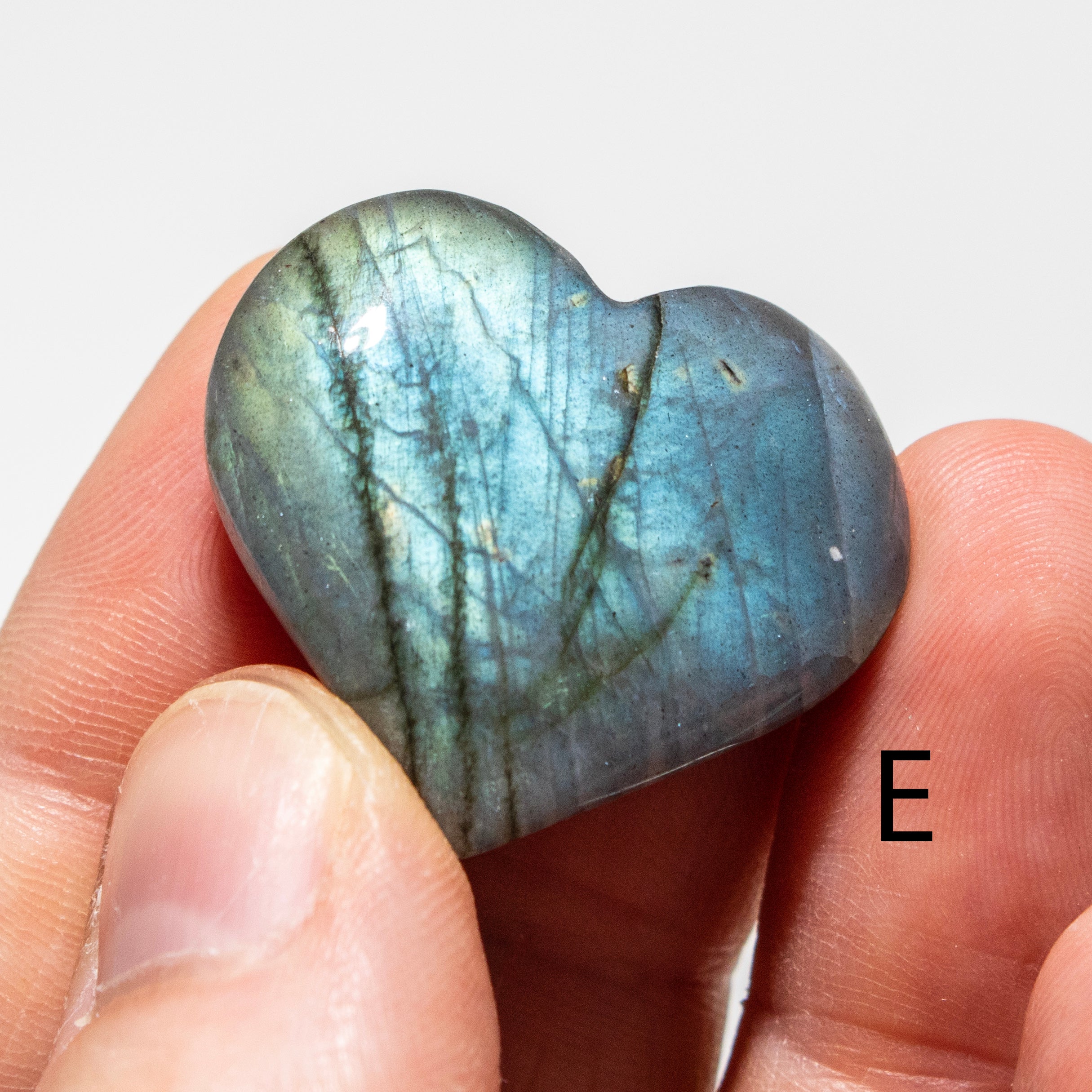 Heart-shaped labradorite stone held between fingers with a blurred background