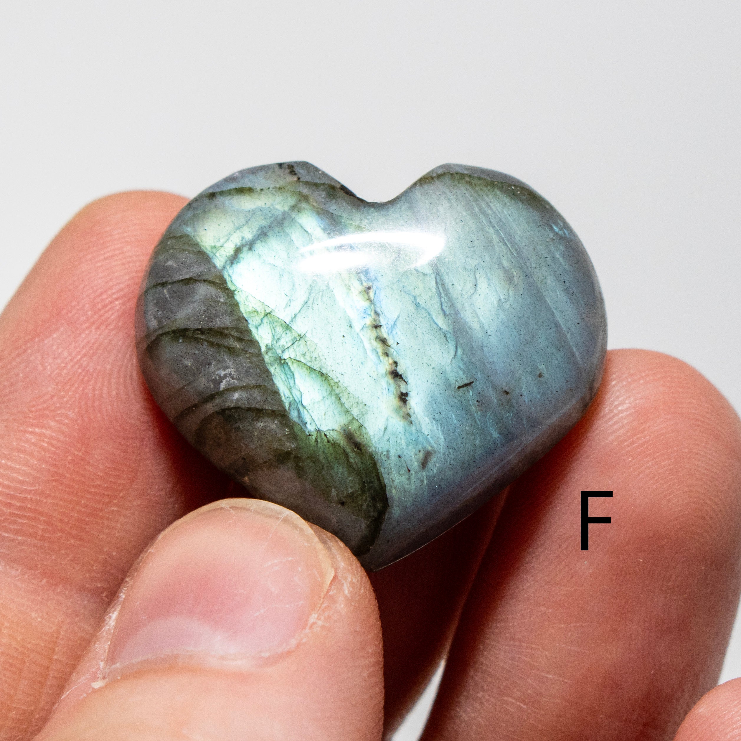 Heart-shaped labradorite stone held between fingers against a white background