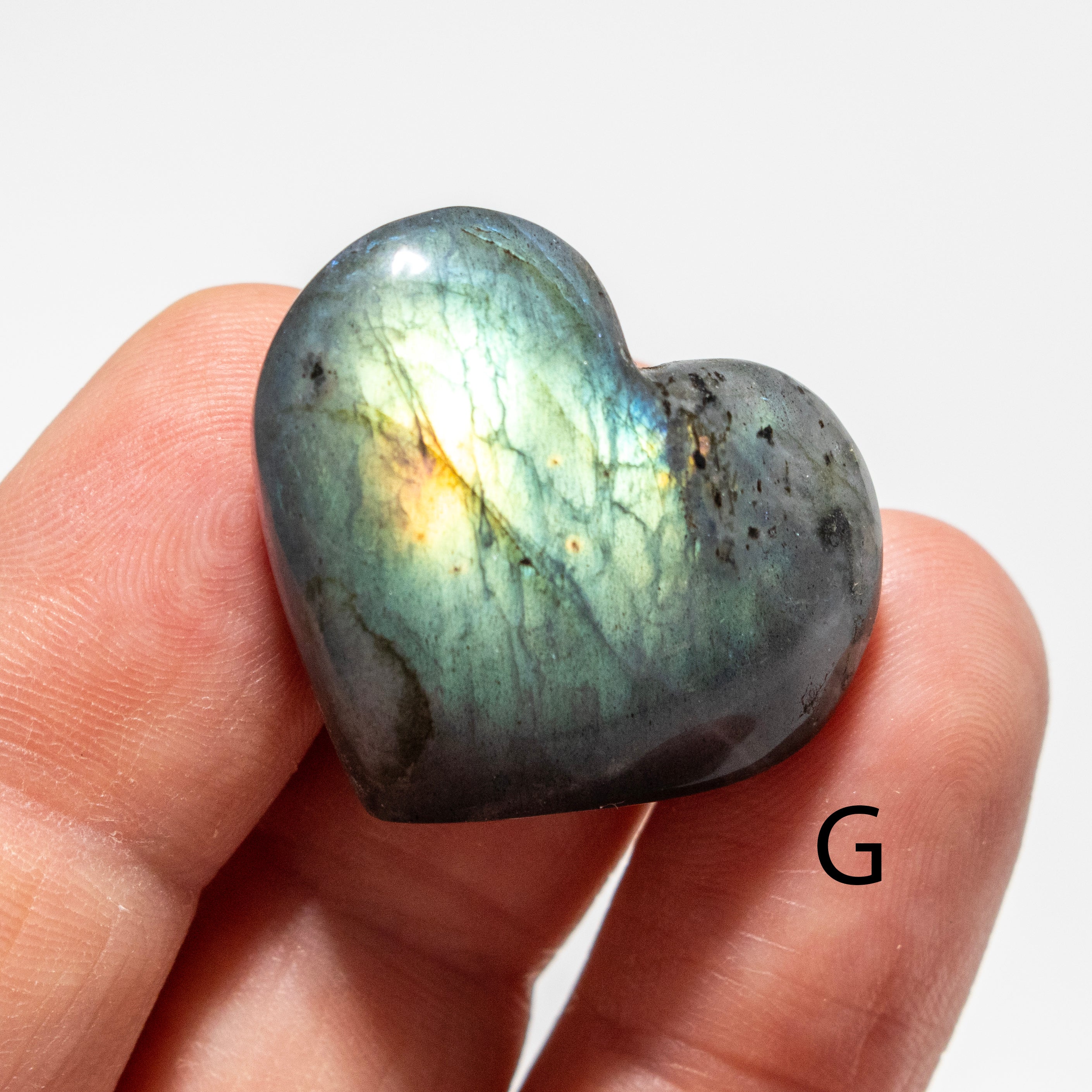 Heart-shaped labradorite stone held in a hand on a white background