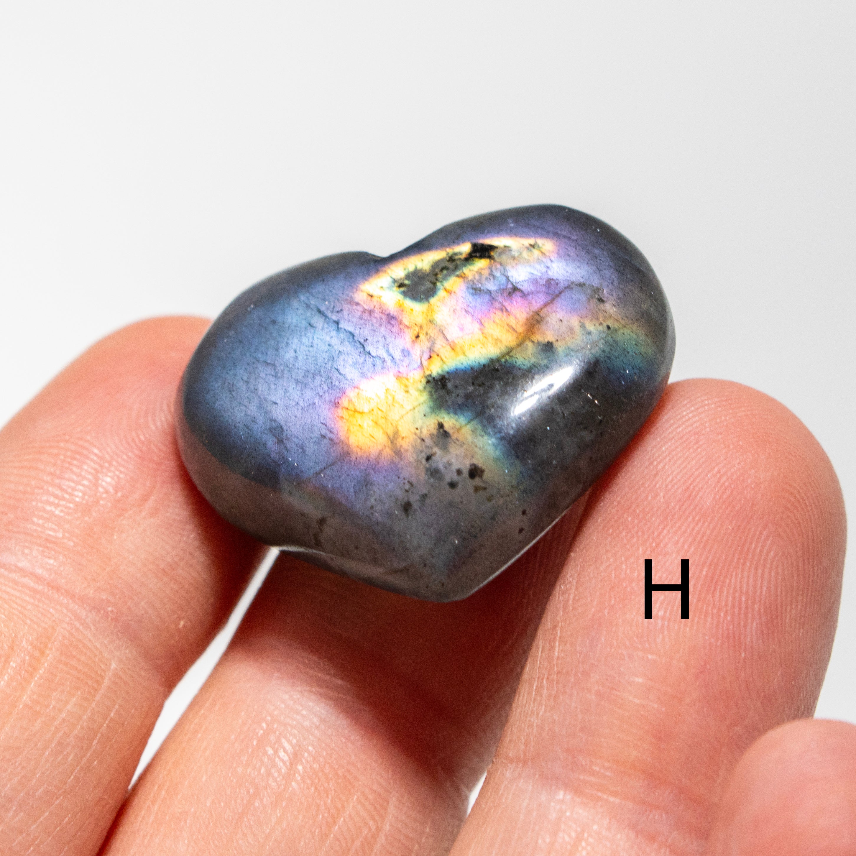 Multicolored labradorite stone held between fingers on a white background