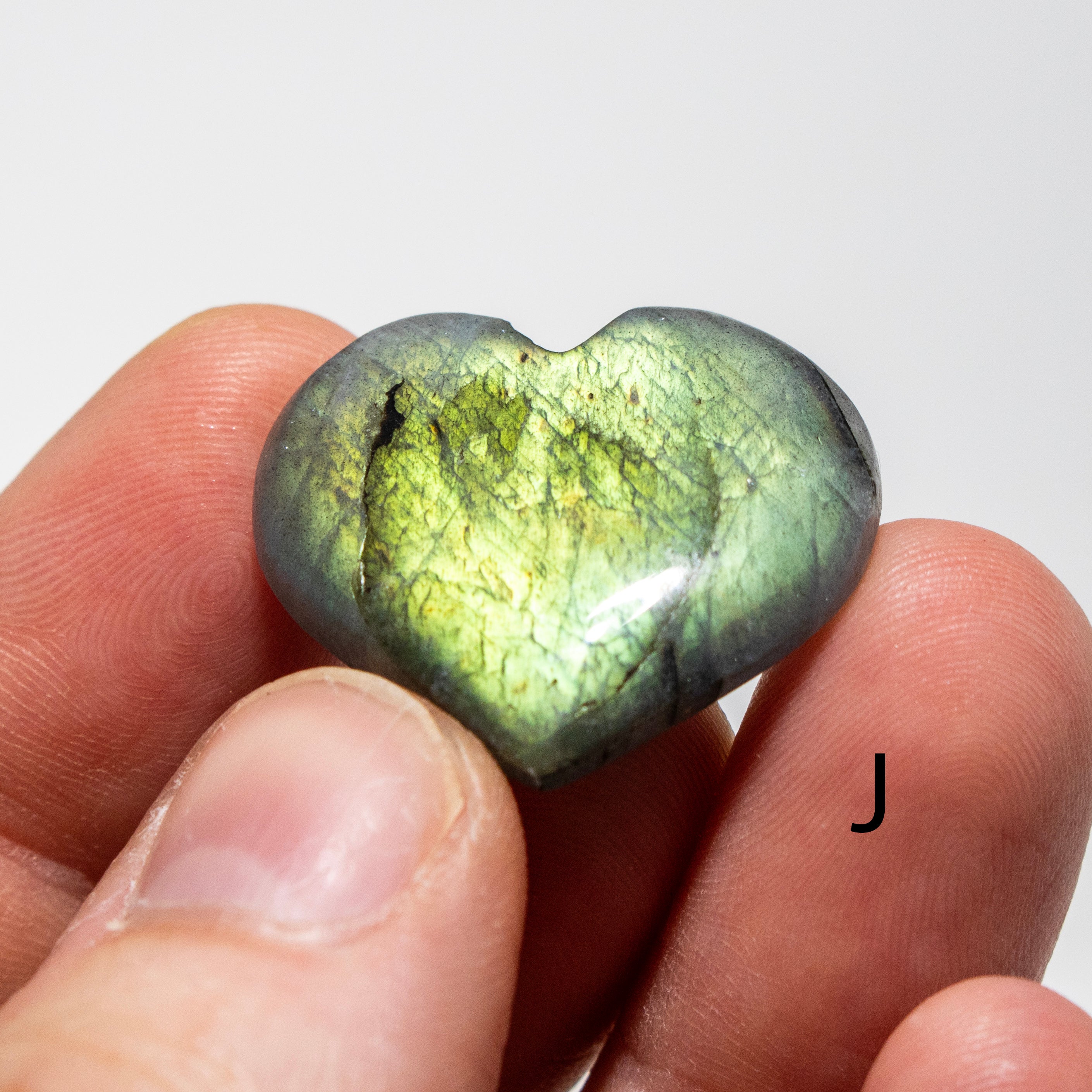Heart-shaped green stone held between fingers against a white background