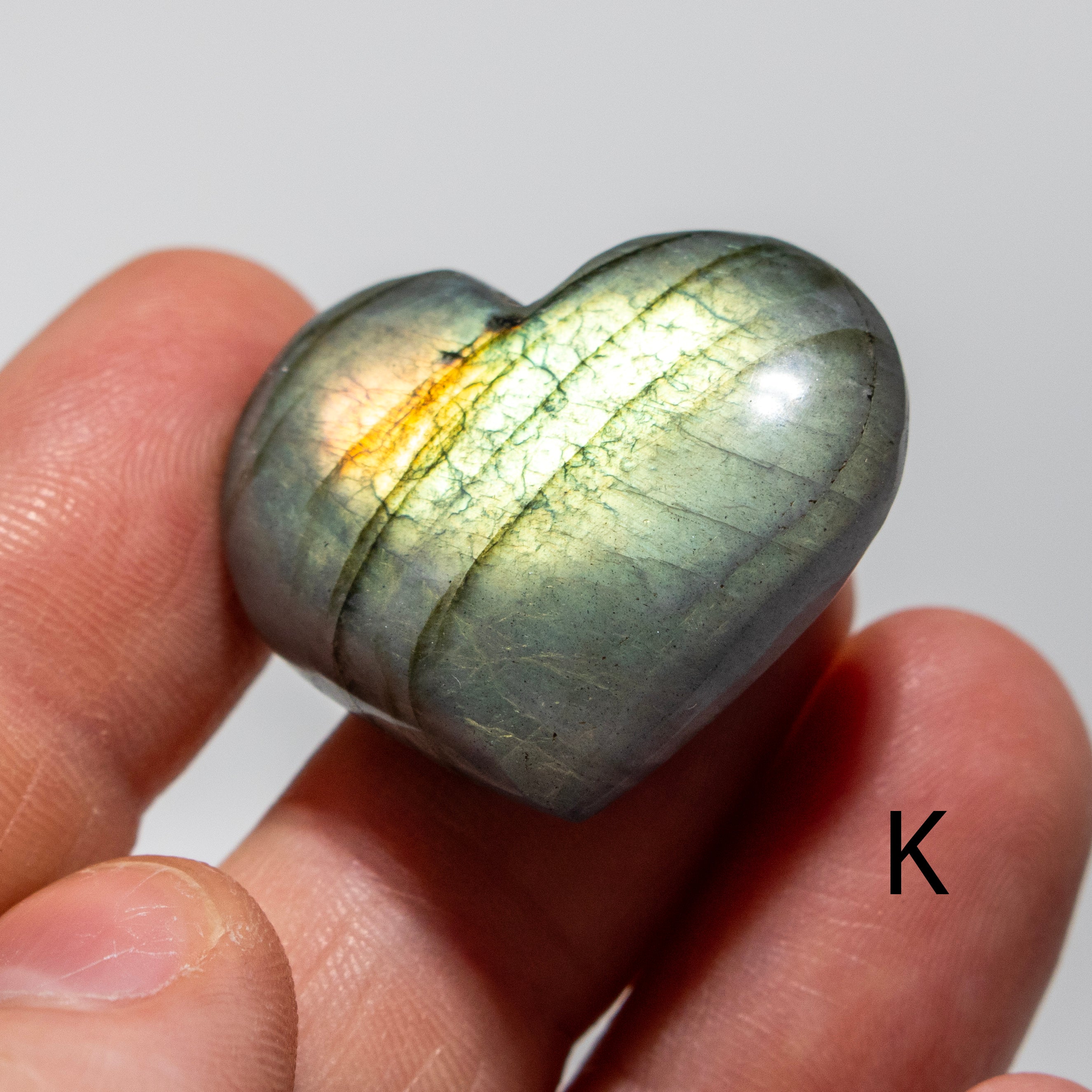 Heart-shaped labradorite stone held in a hand against a plain background