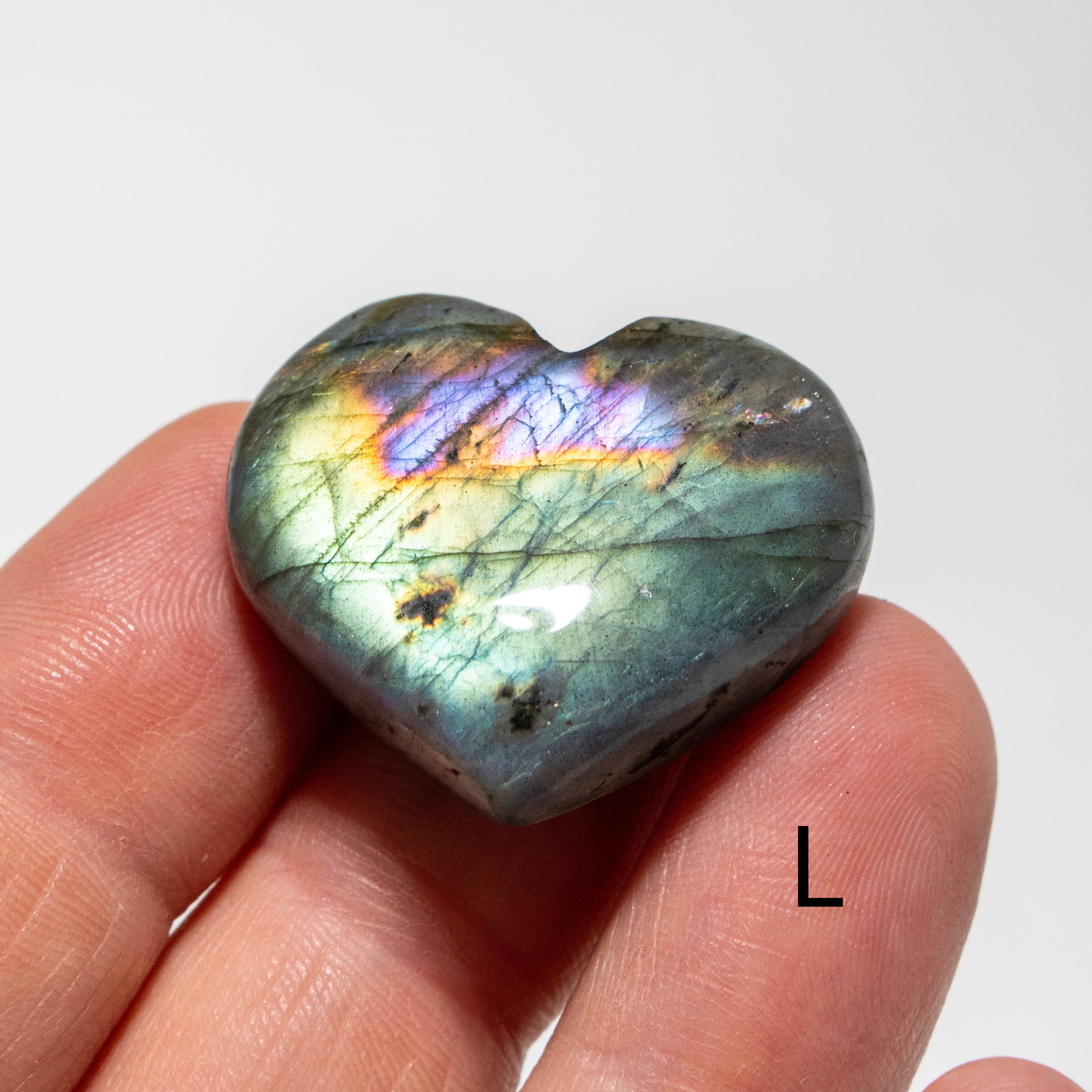 Heart-shaped labradorite stone held in a hand against a white background