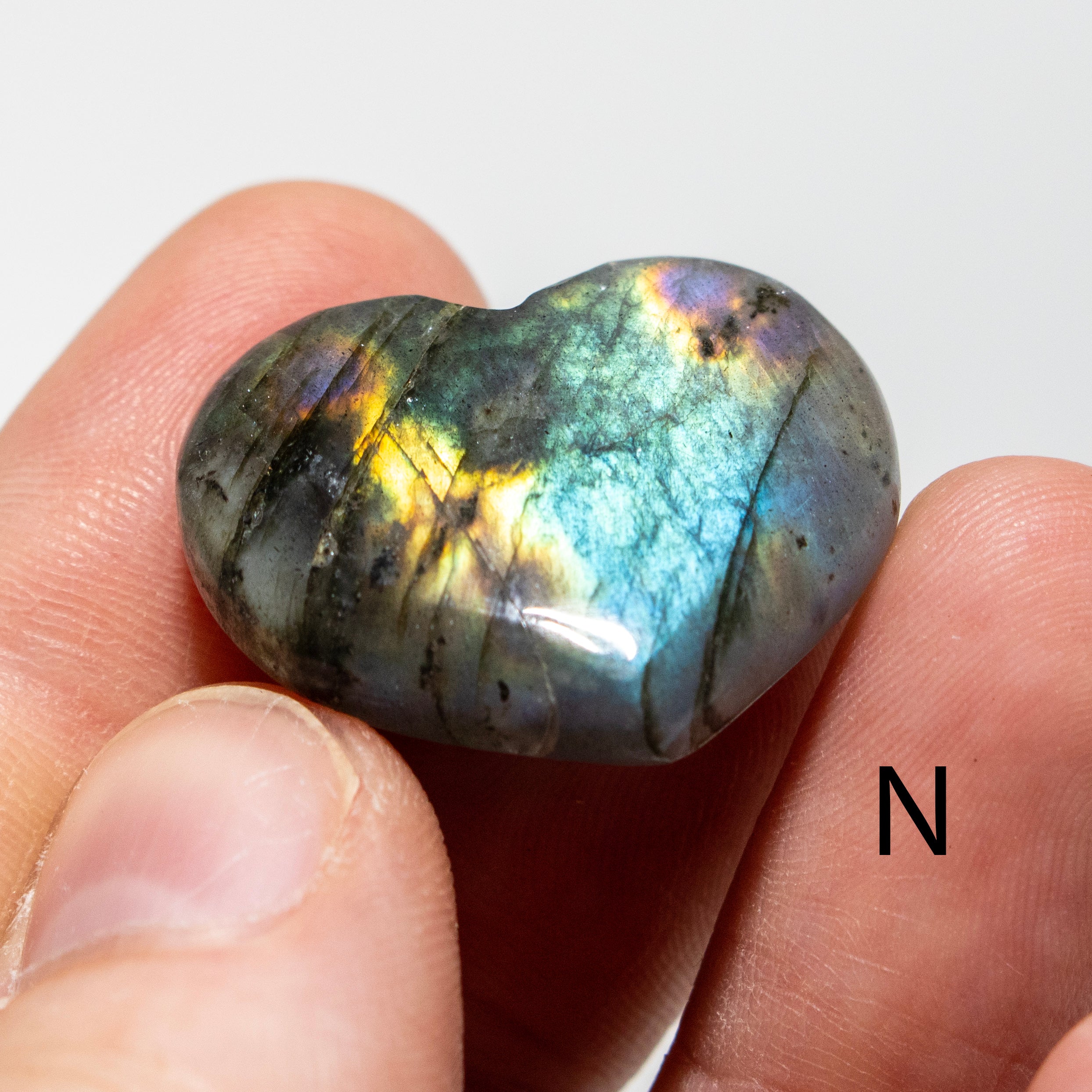 Heart-shaped labradorite stone held between fingers on a white background