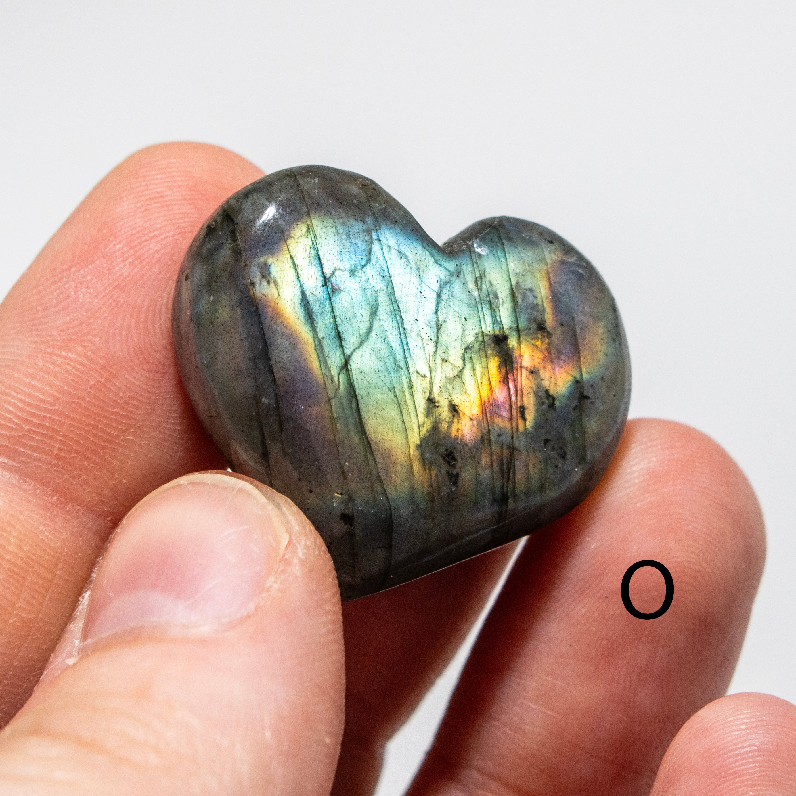Heart-shaped labradorite stone held between fingers against a white background