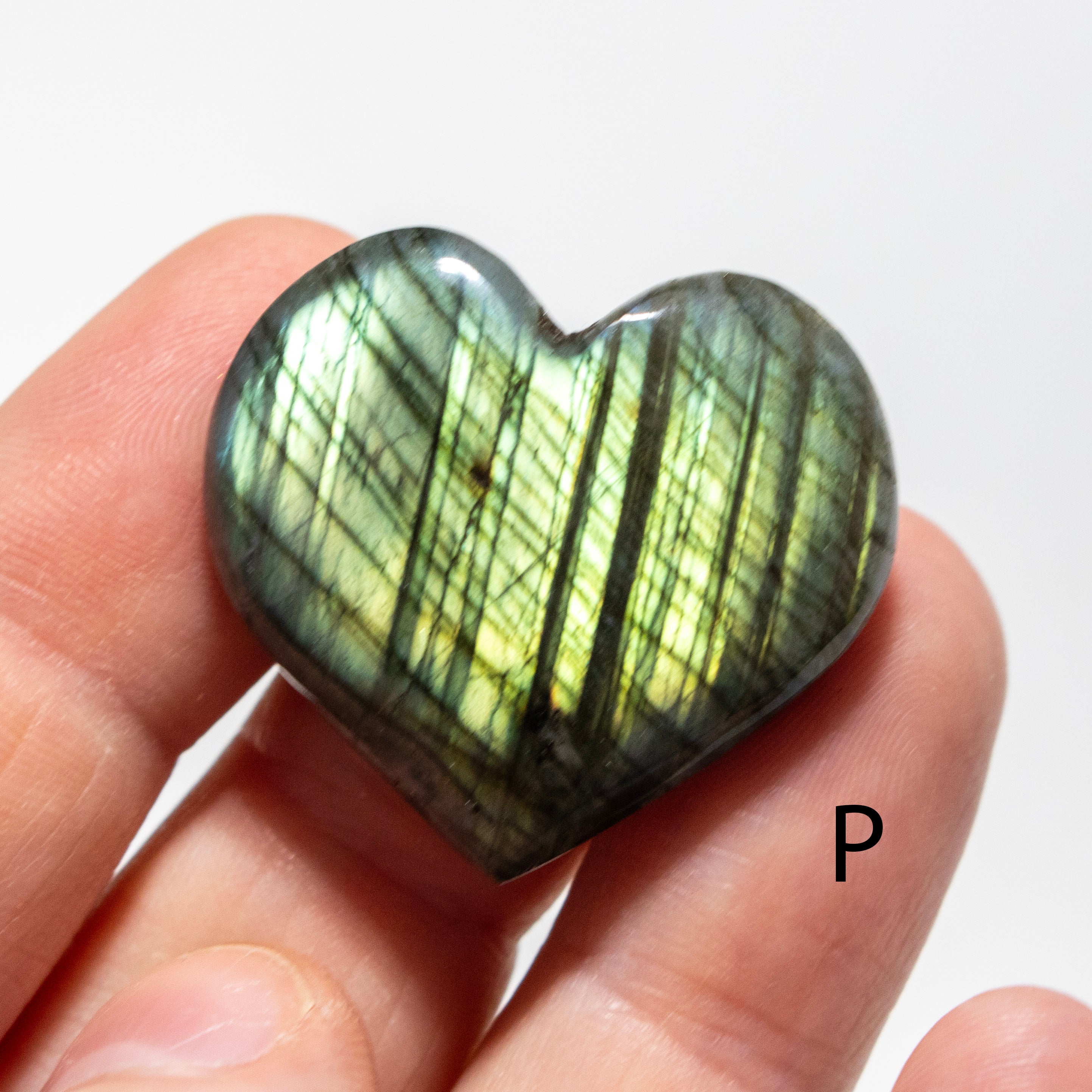 Heart-shaped labradorite stone held in a hand against a white background
