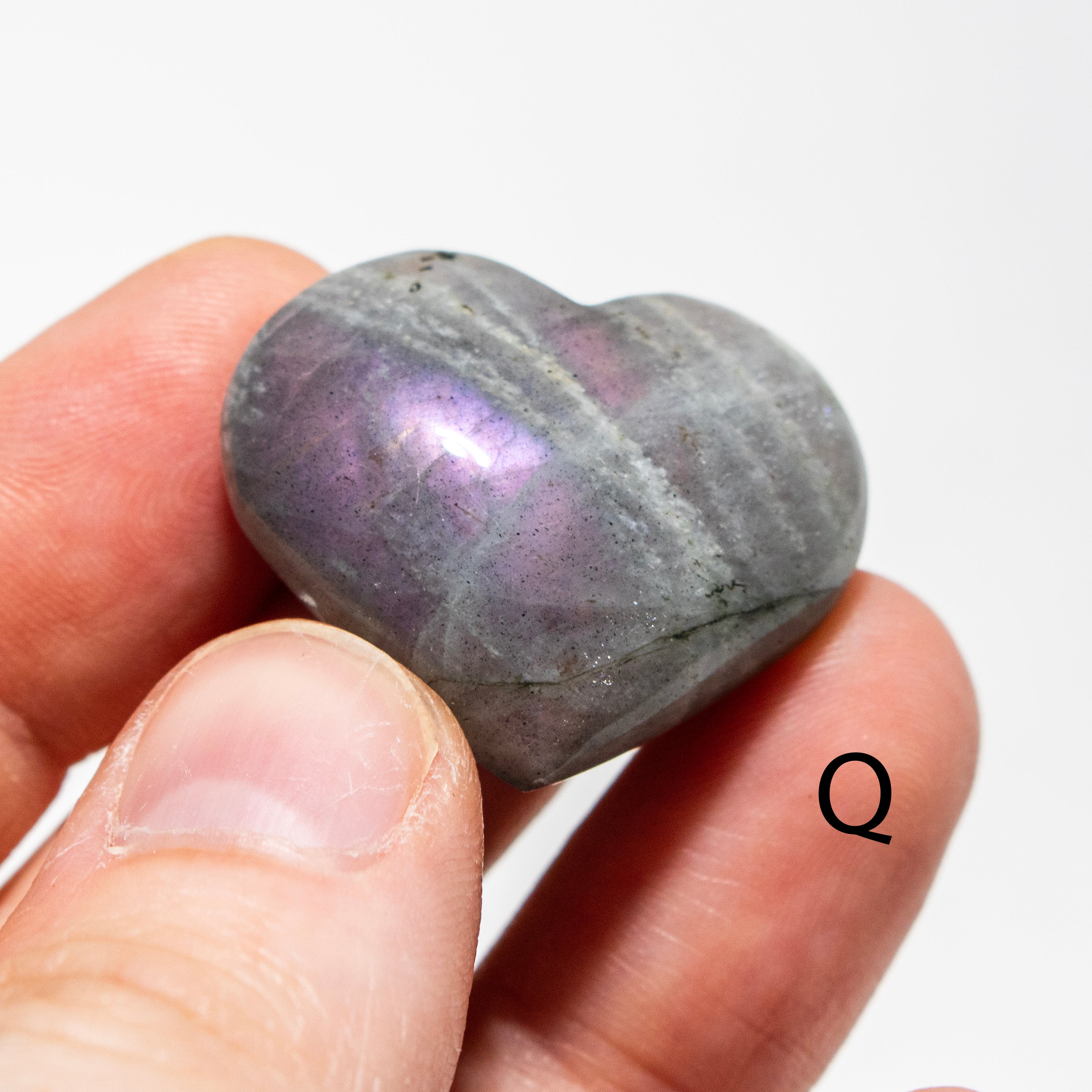 Heart-shaped stone held between fingers with a white background