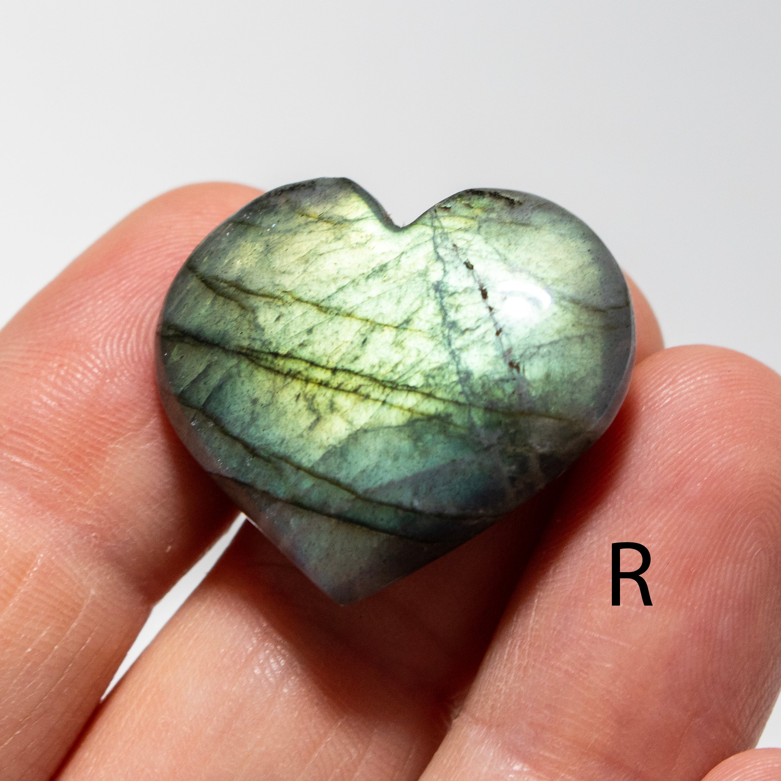 Heart-shaped labradorite stone held in a hand with a white background