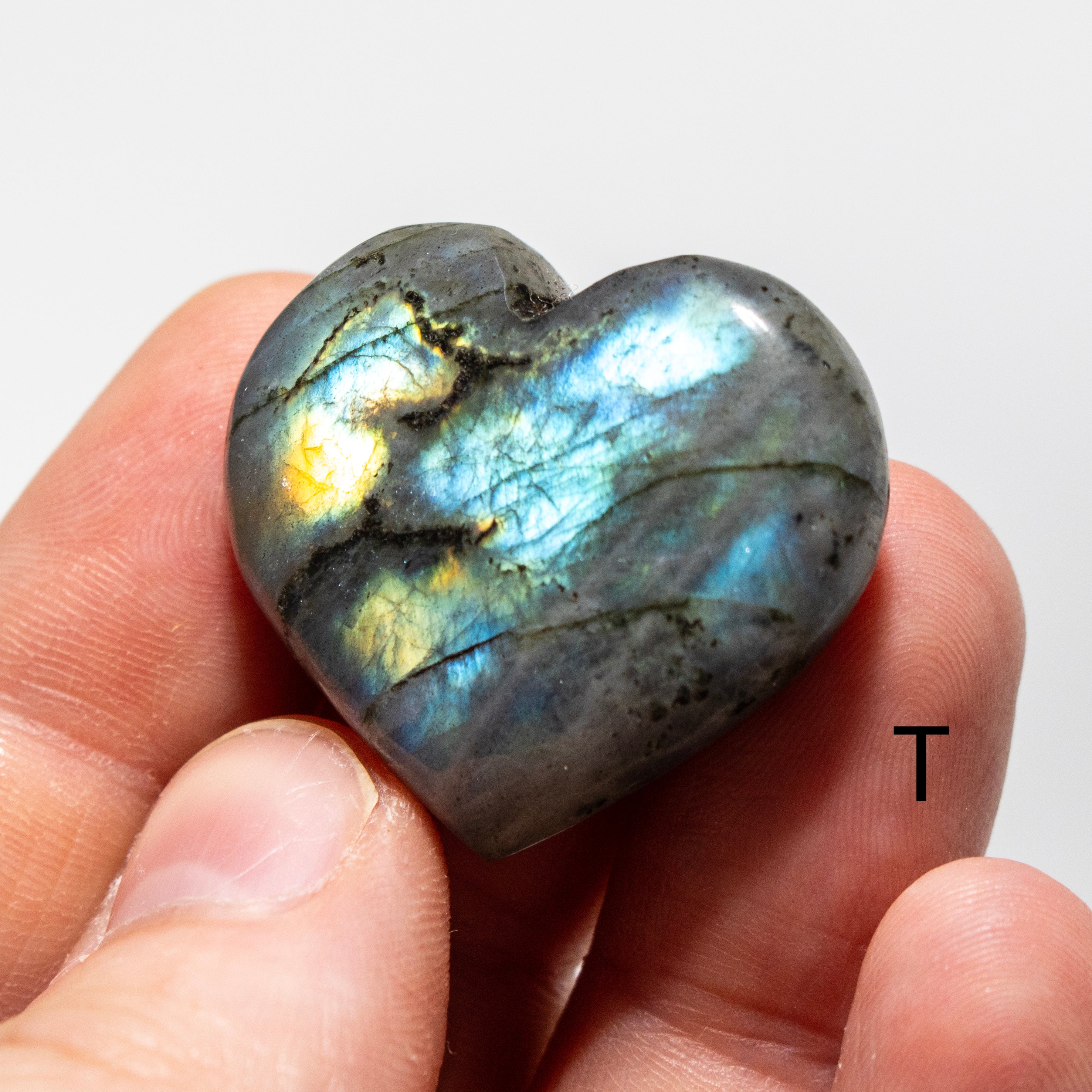Heart-shaped labradorite stone held in a hand against a white background