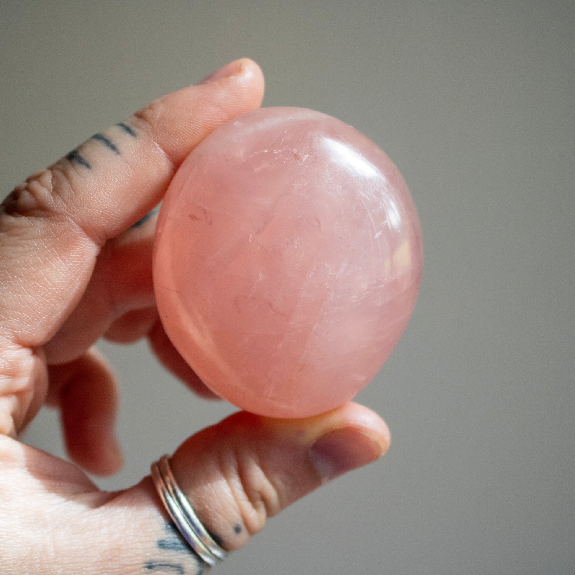 Hand holding a pink stone against a neutral background
