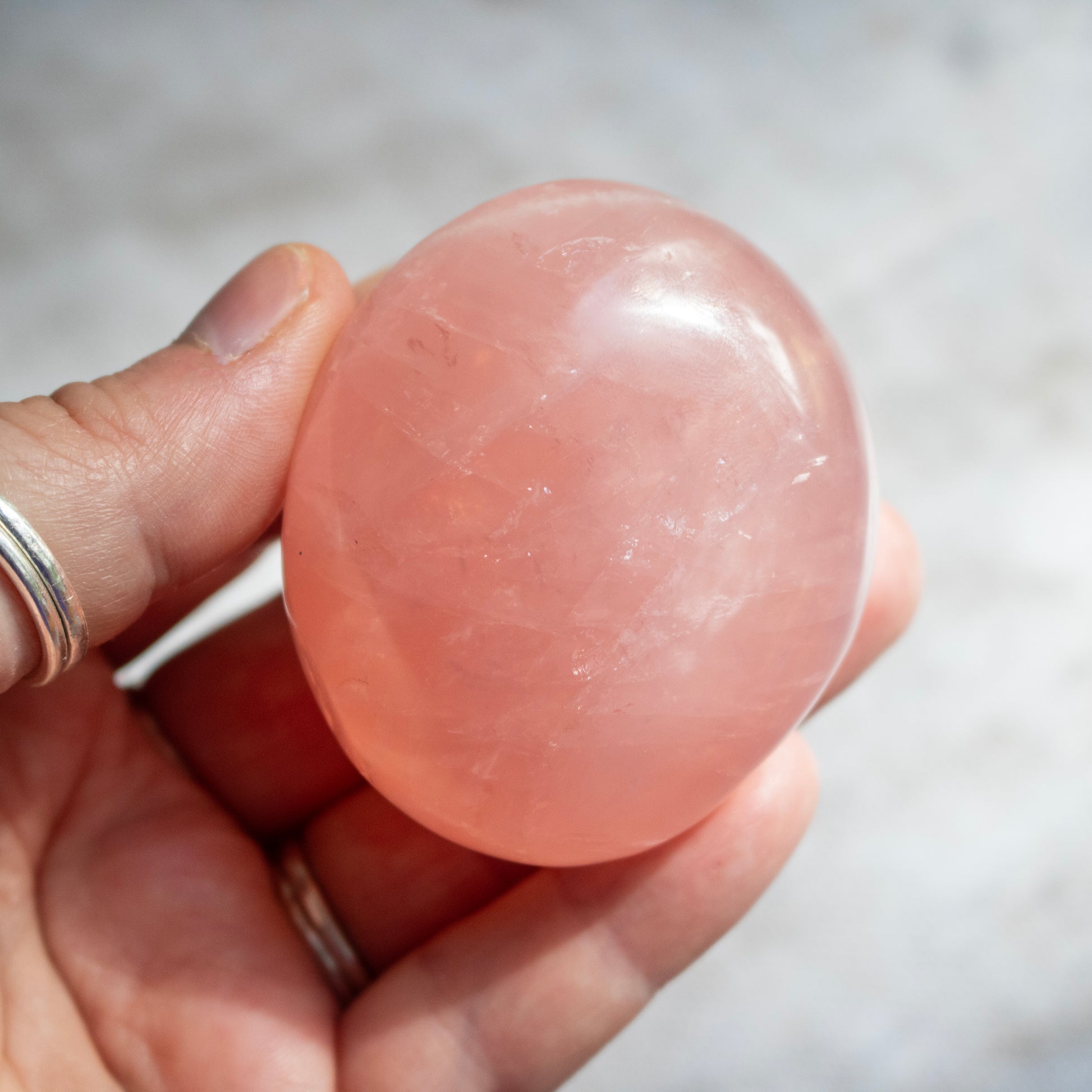 Hand holding a pink stone against a neutral background