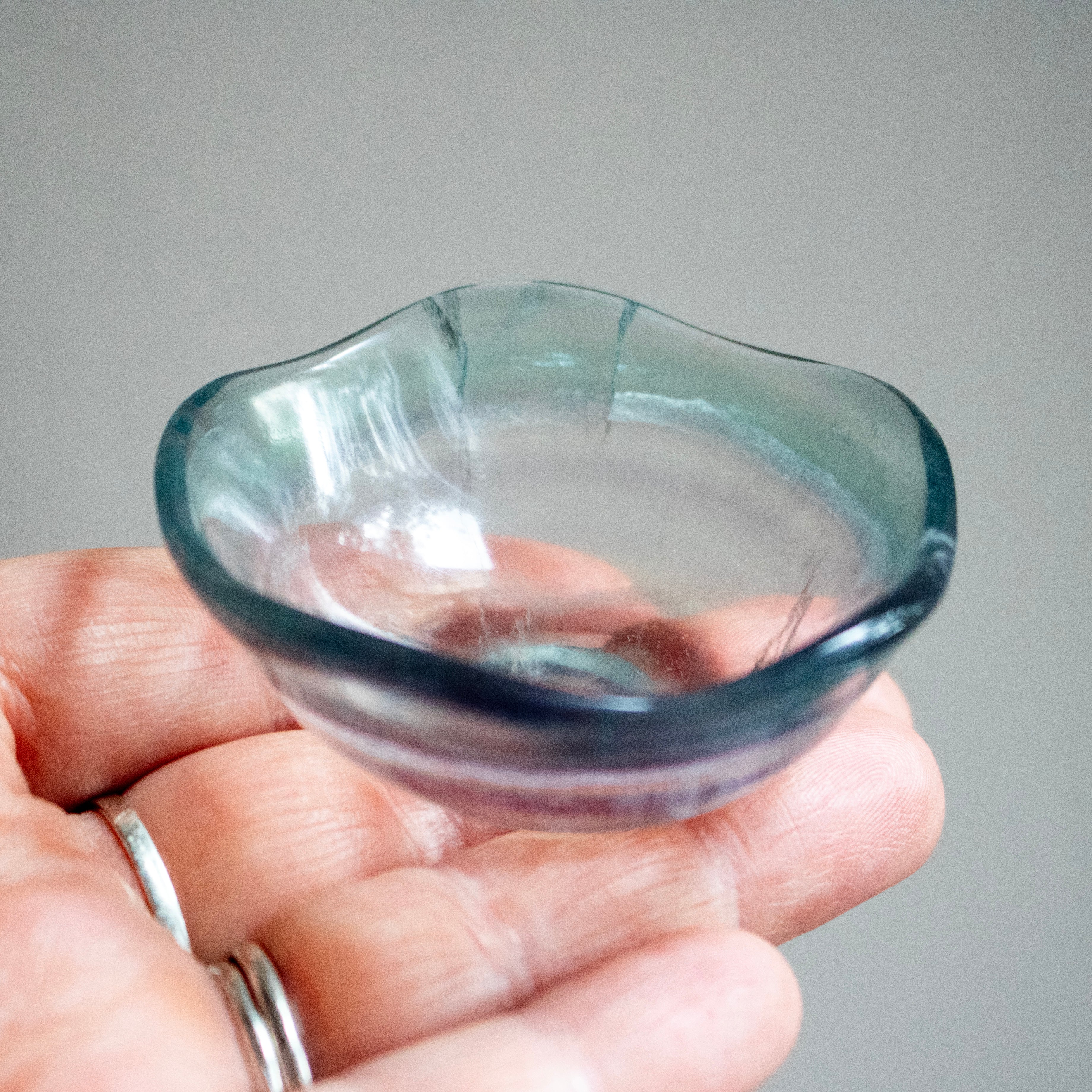 Hand holding a small crystal bowl with a cracked rim against a gray background