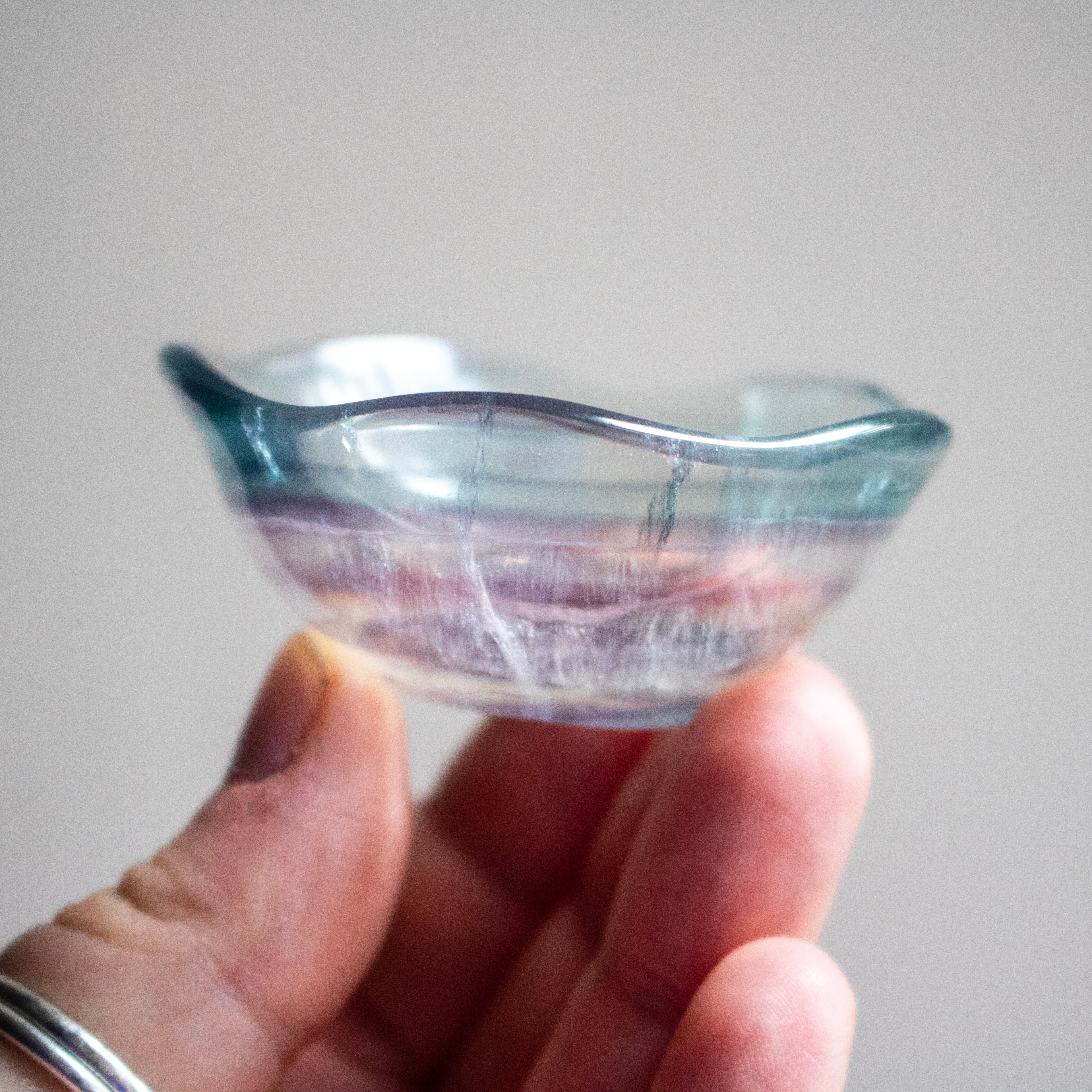 Hand holding a small crystal bowl with a wavy rim against a plain background