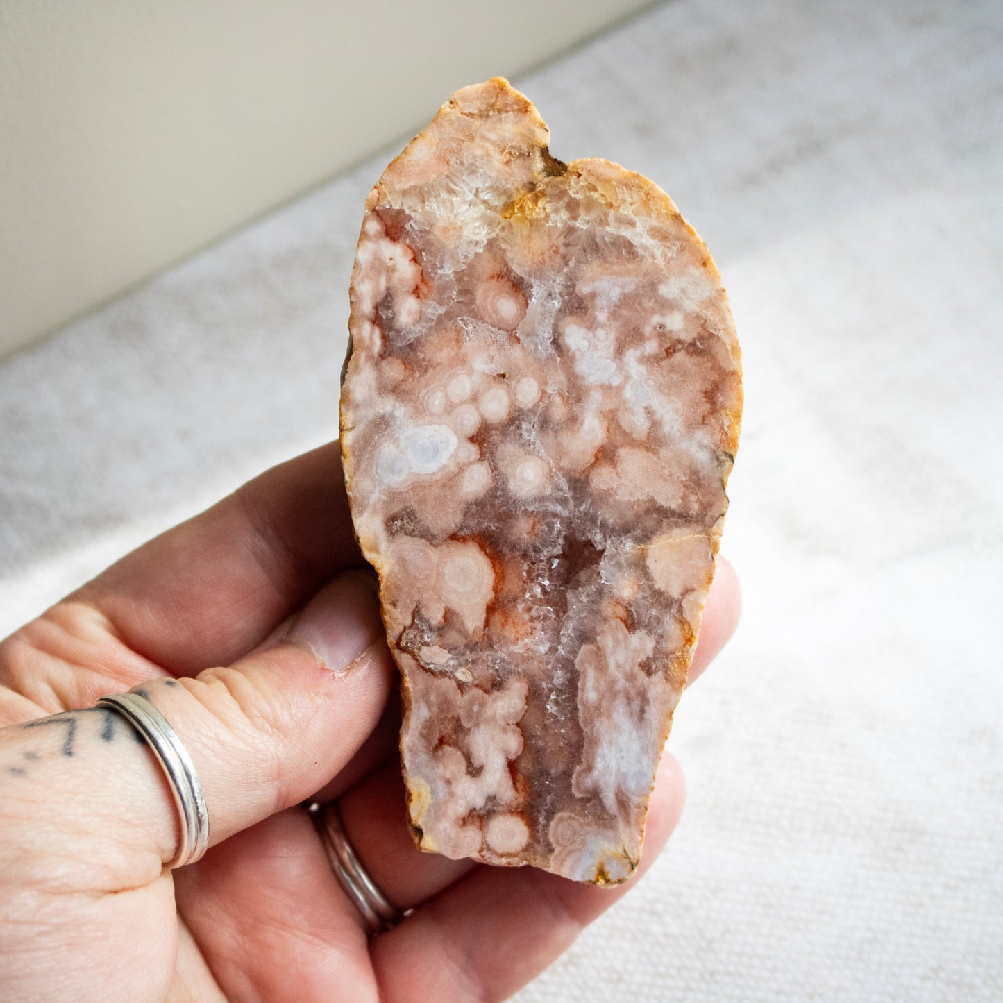 Hand holding a rough-cut crystal or mineral specimen on a neutral background
