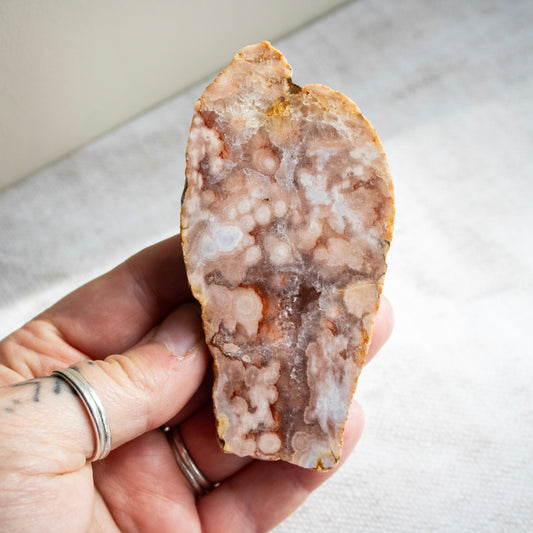 Hand holding a rough-cut crystal or mineral specimen on a neutral background