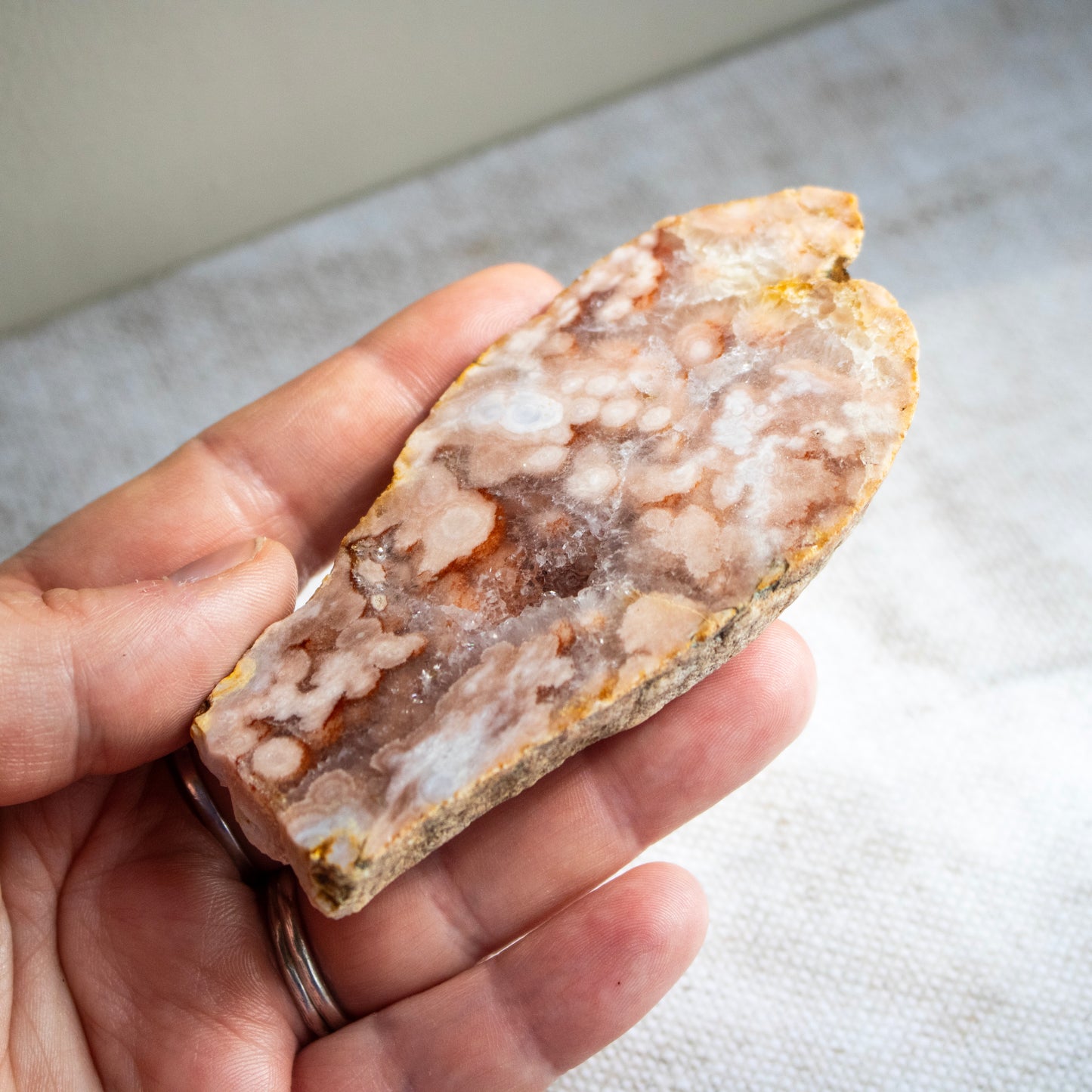 Hand holding a rough-cut crystal or mineral stone with a pattern of colors.