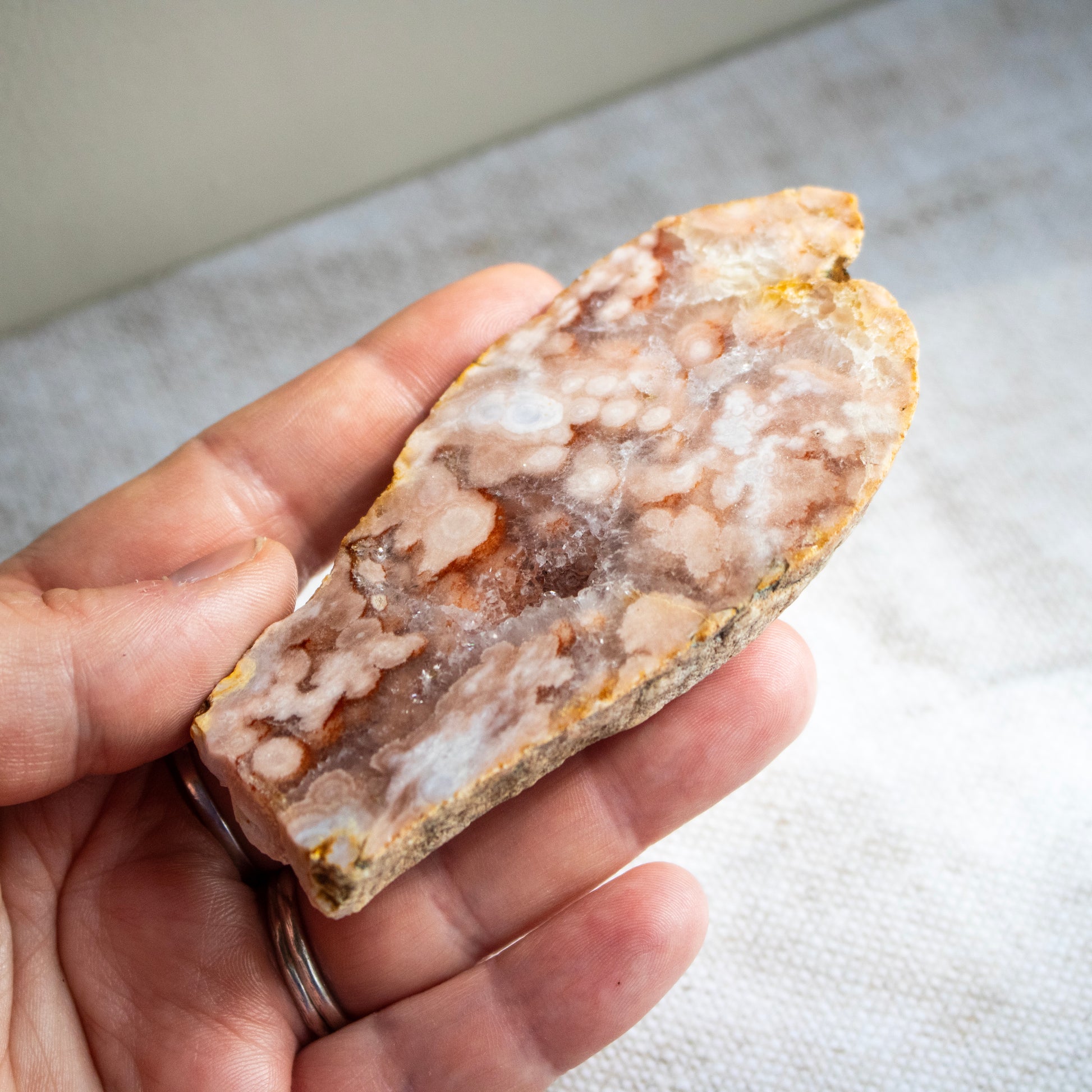 Hand holding a rough-cut crystal or mineral stone with a pattern of colors.