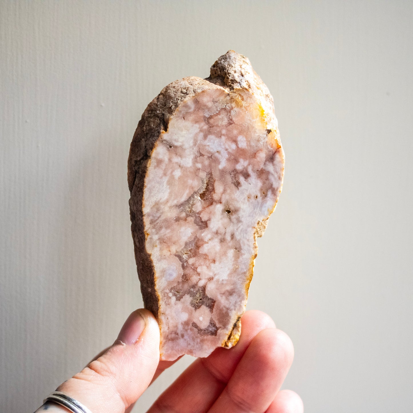Hand holding a geode with a light interior against a neutral background