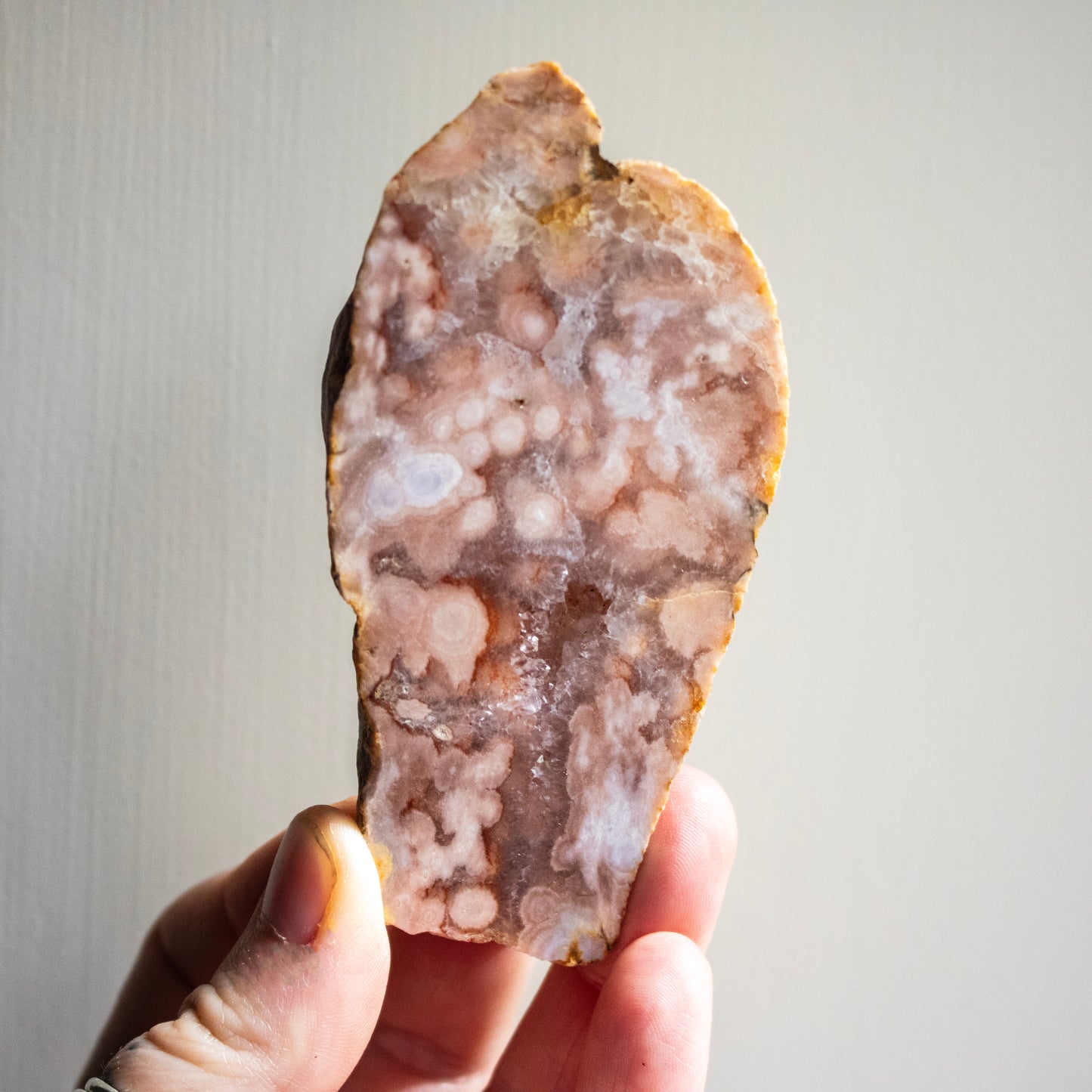 Hand holding a large, polished agate stone against a neutral background