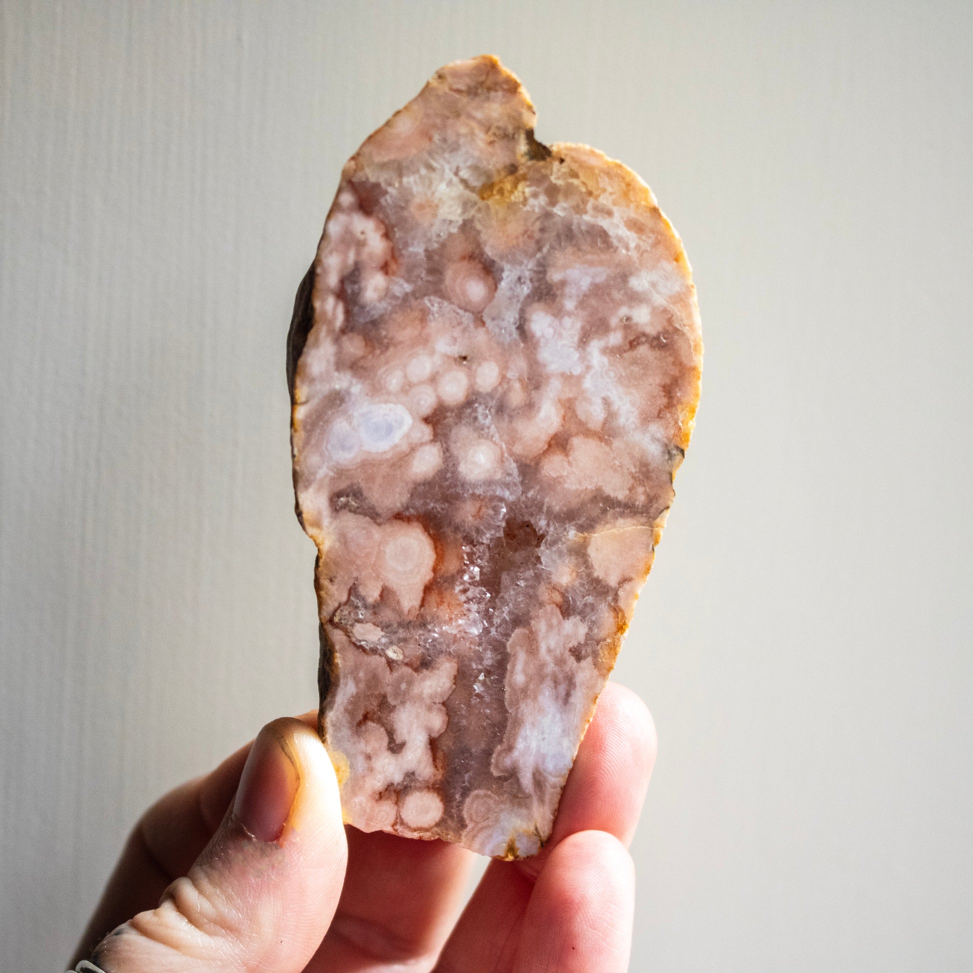 Hand holding a large, polished agate stone against a neutral background