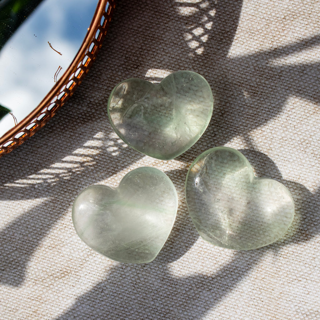 Three green heart-shaped stones on a textured surface with a woven basket in the background.