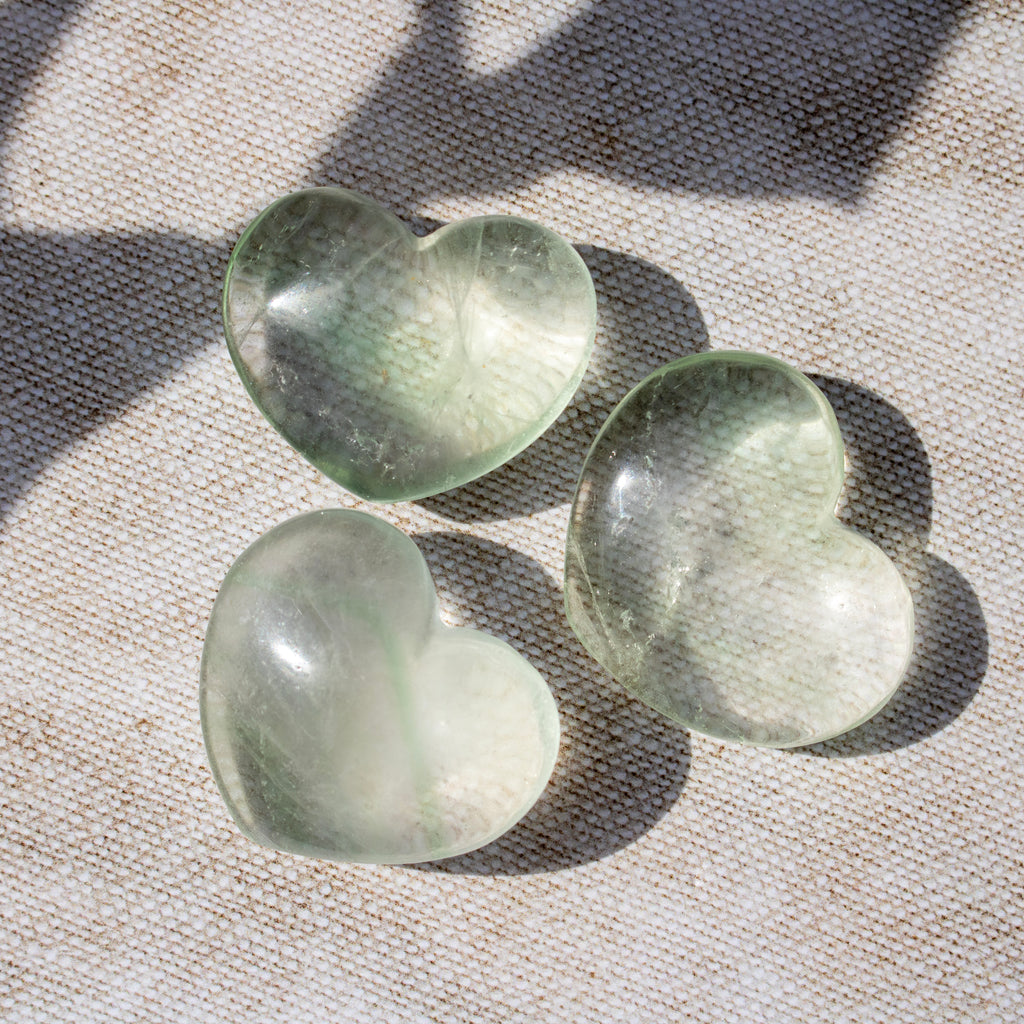 Three green heart-shaped stones on a textured fabric background