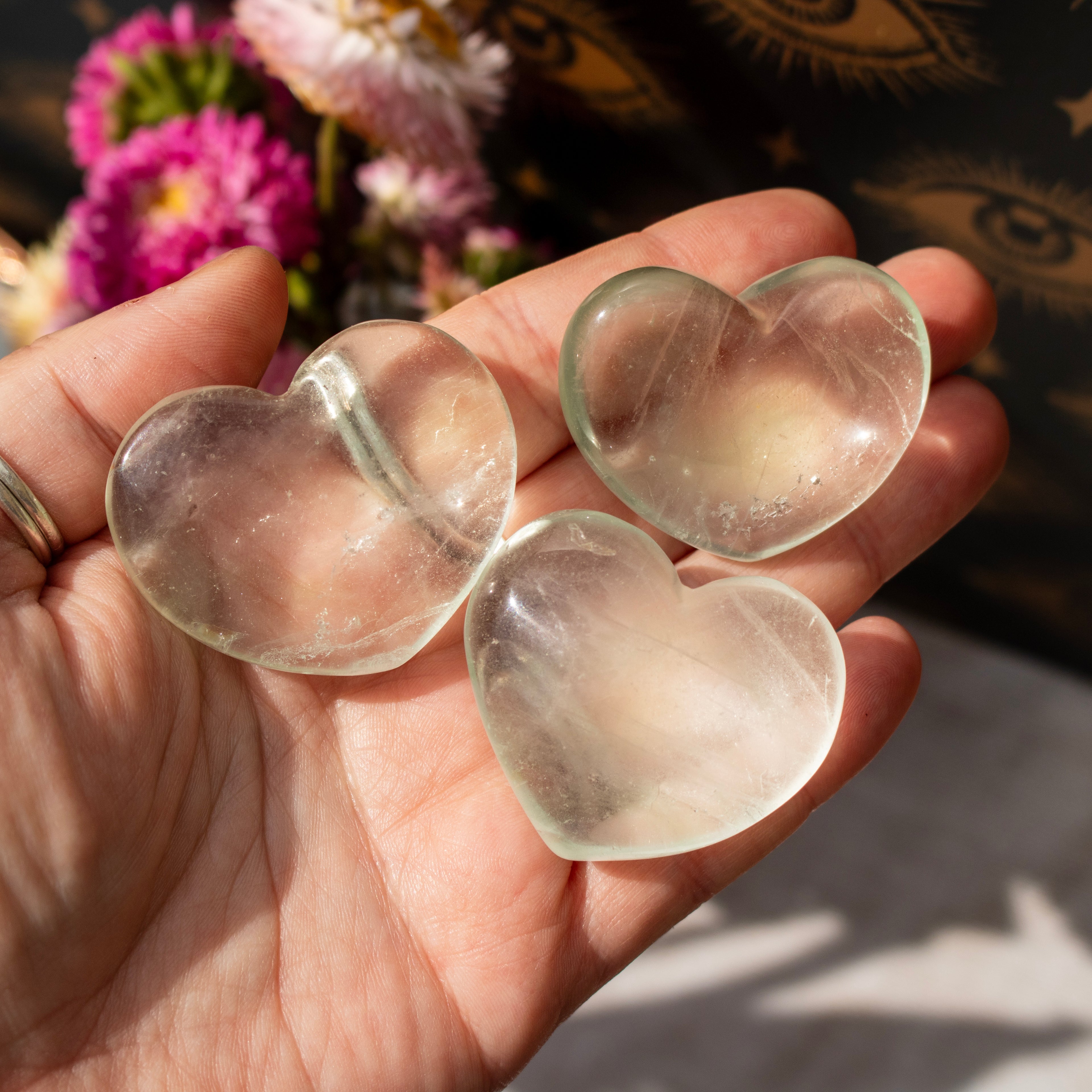 Three clear heart-shaped stones held in a hand with a blurred floral background
