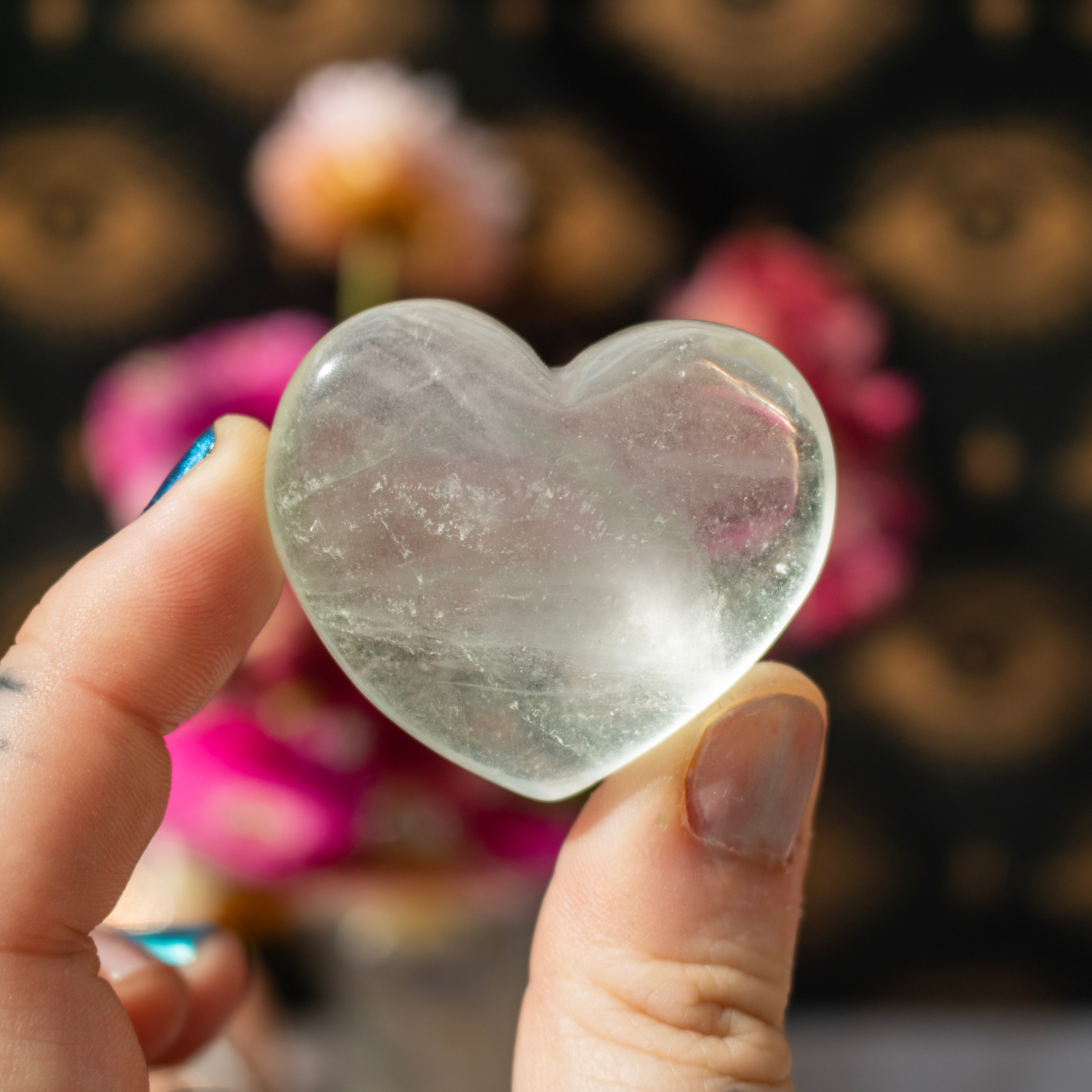 Heart-shaped crystal held by a hand with a blurred floral background