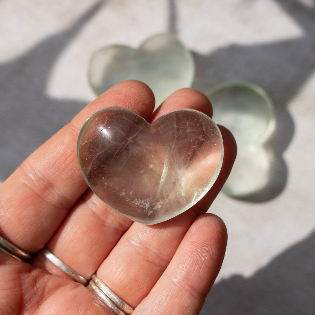 Heart-shaped clear crystal held in a hand with a neutral background