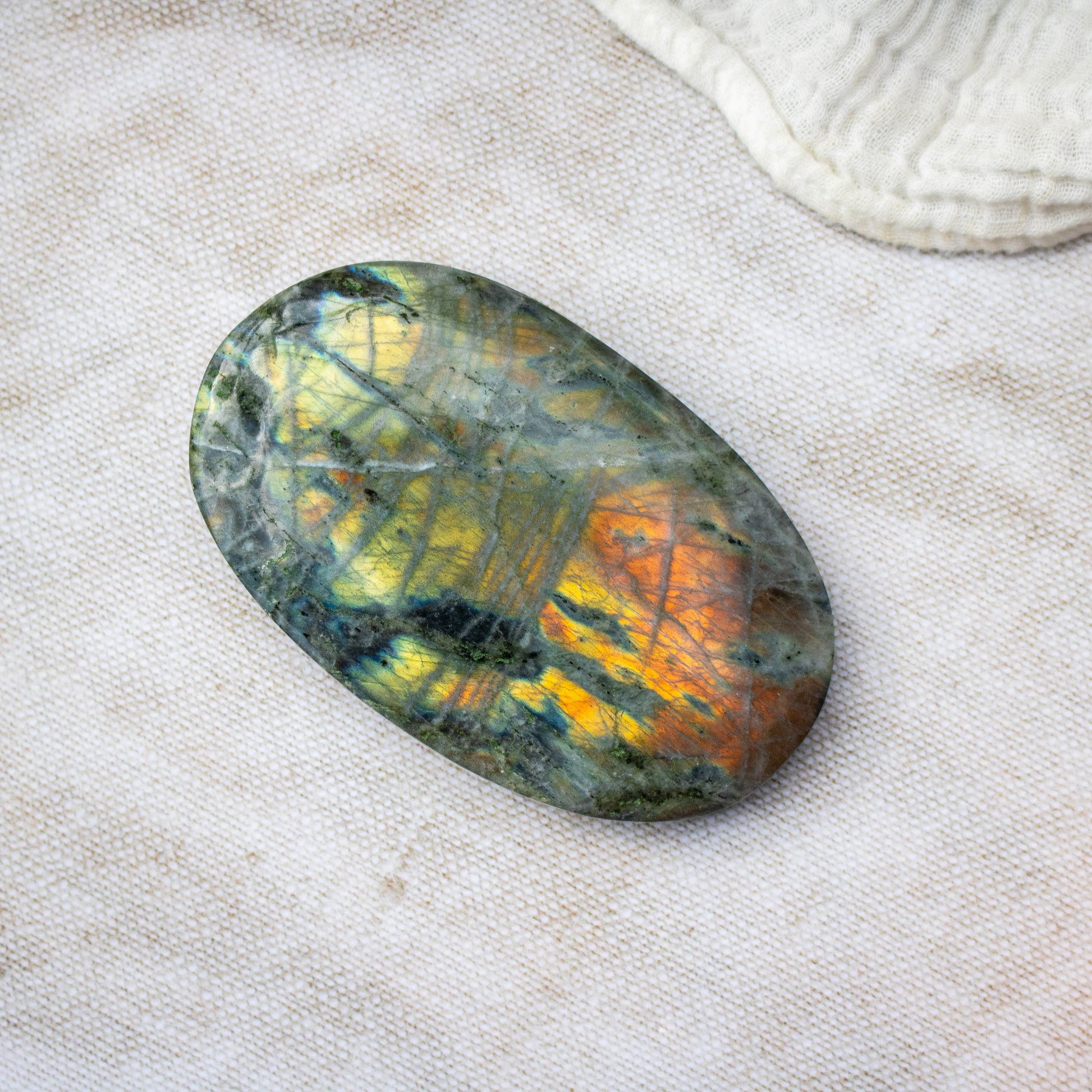Oval-shaped labradorite stone on a textured beige surface