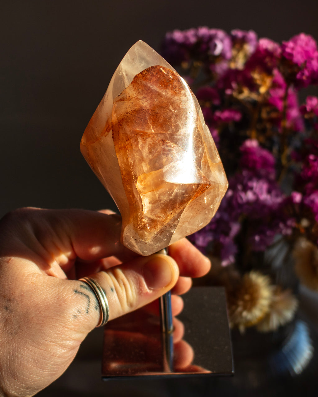 Hand holding a large crystal with a blurred background of flowers