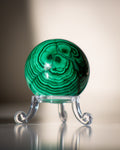 Green malachite sphere on a clear stand against a neutral background
