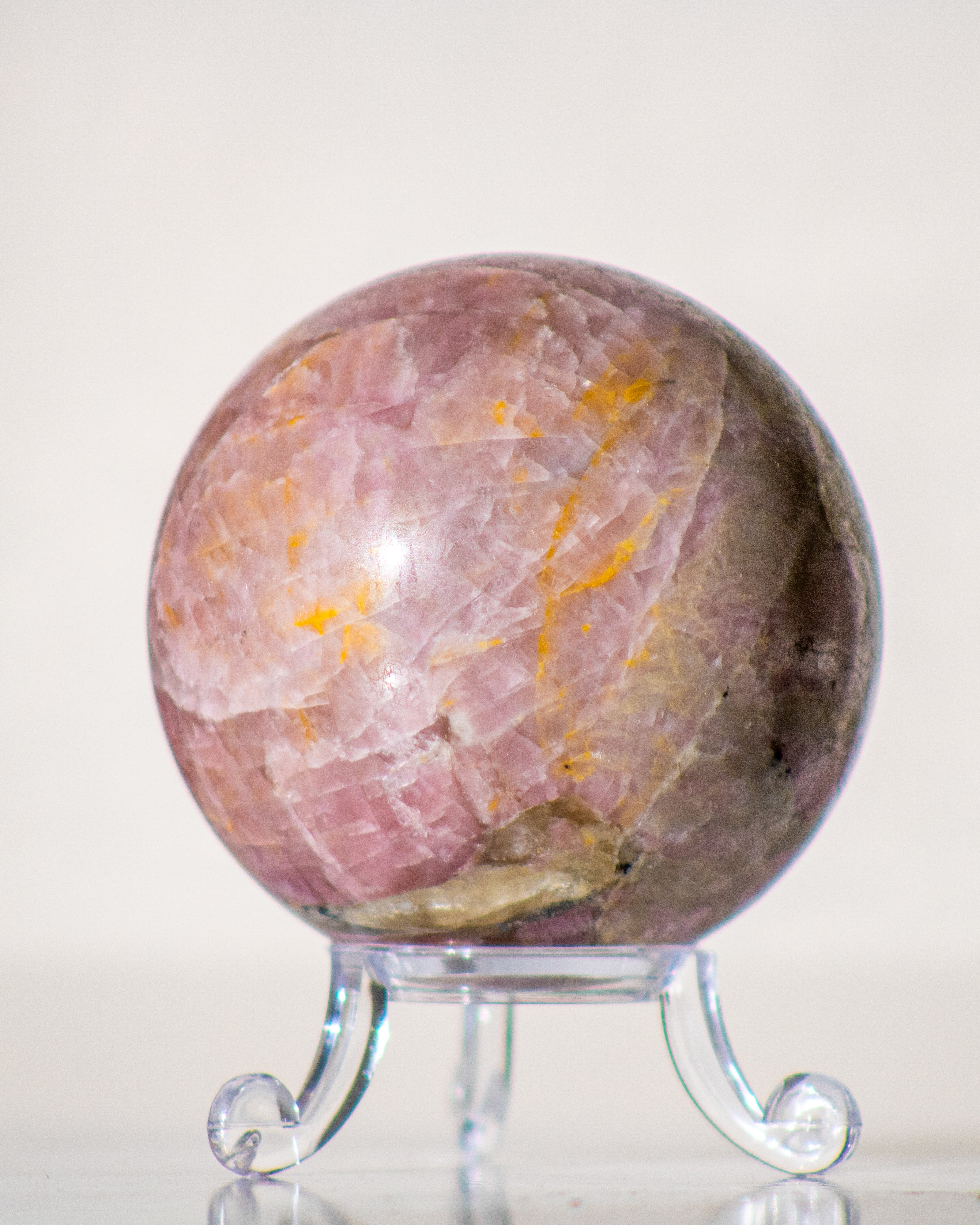 Marbled pink and orange tourmaline stone  sphere on a clear stand against a white background