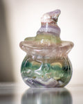 a purple and green fluorite crystal carved to look like a pumpkin with a hollowed out ace wearing a pointed witch's hat