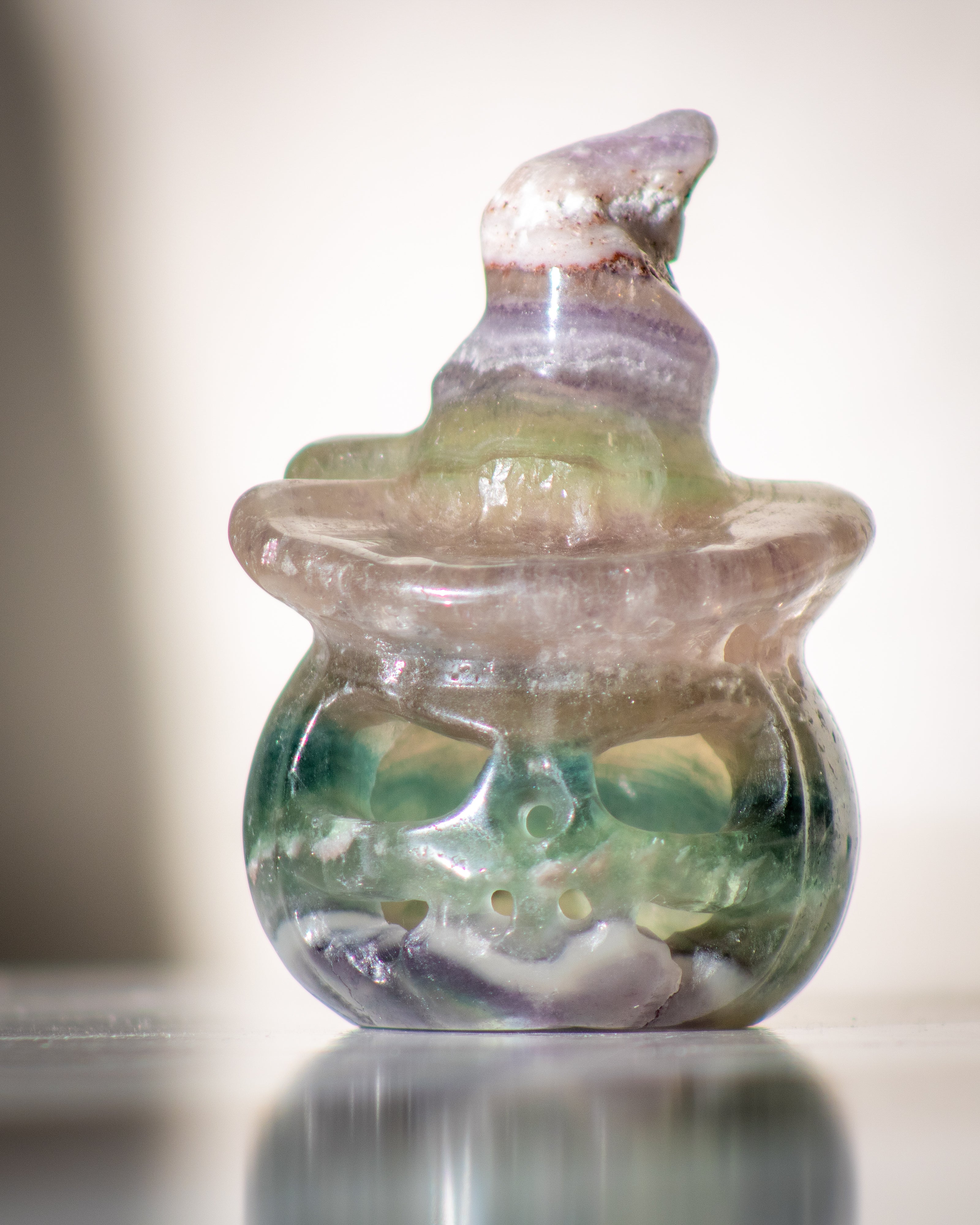 a purple and green fluorite crystal carved to look like a pumpkin with a hollowed out ace wearing a pointed witch's hat