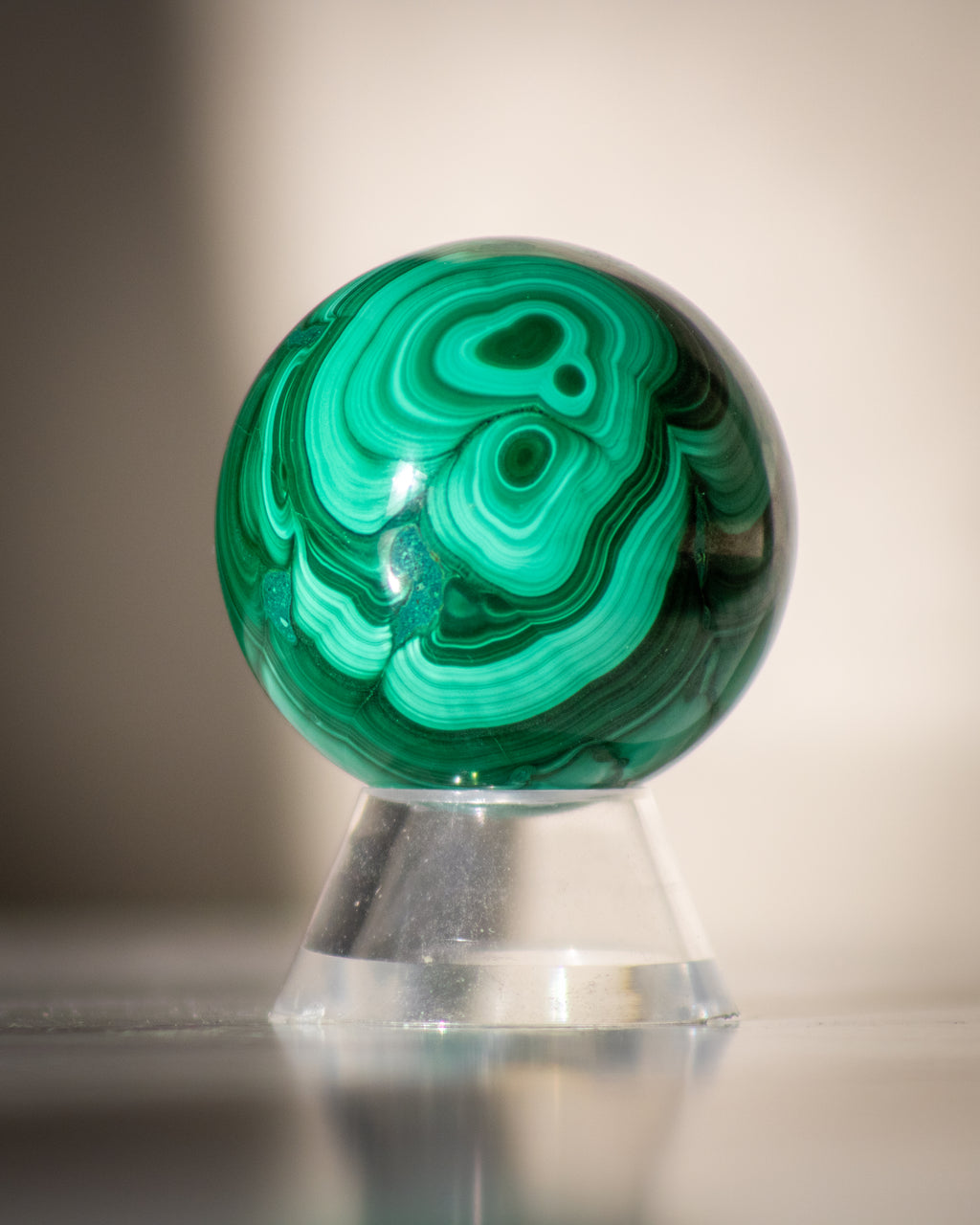 Green malachite sphere on a stand against a neutral background