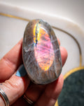 Hand holding a colorful stone with a rainbow-like pattern against a blurred background