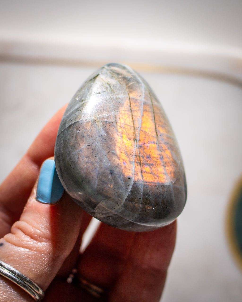 Person holding a teardrop-shaped labradorite stone with a reflective surface.