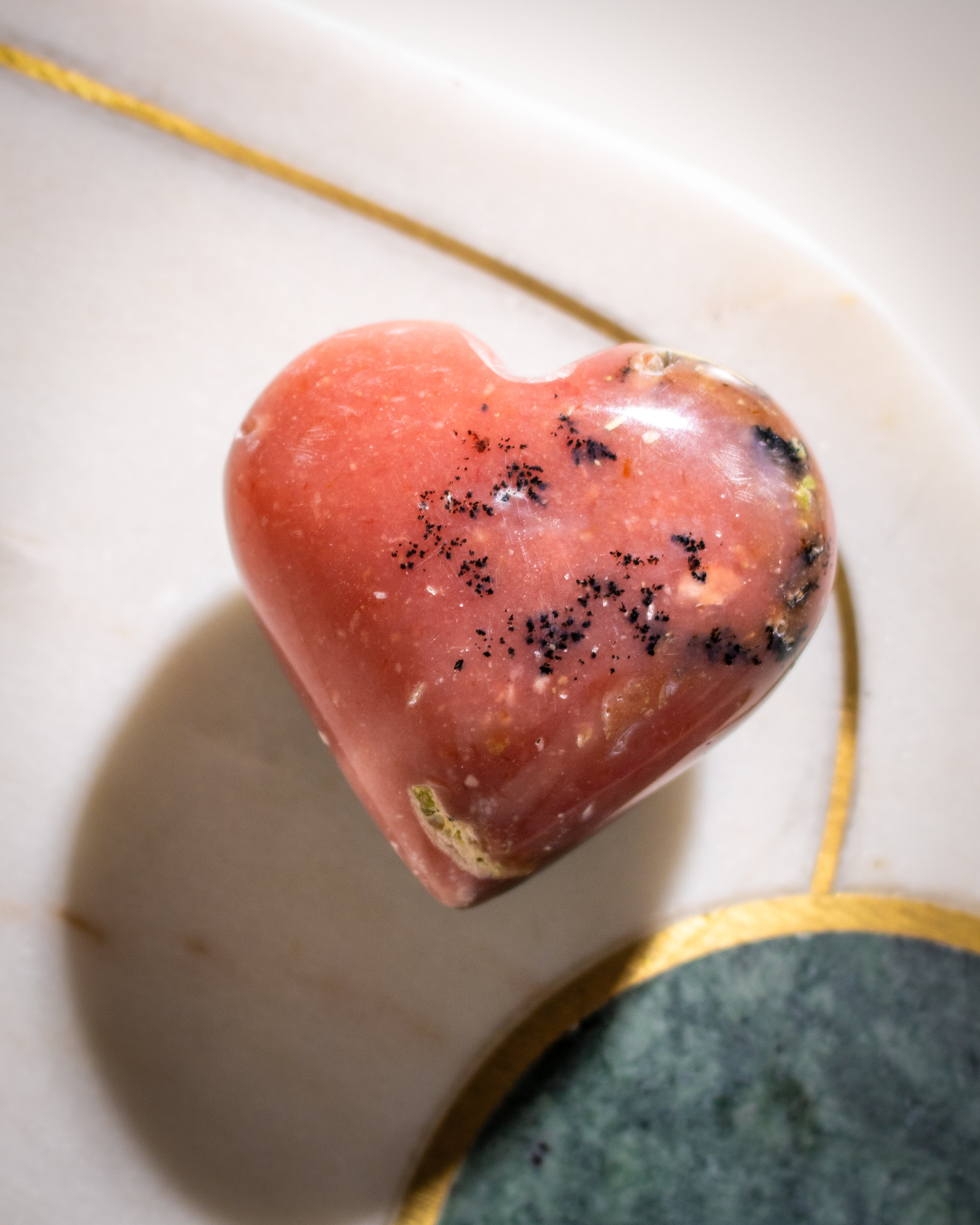 Heart-shaped pink stone with black specks on a white plate with gold rim