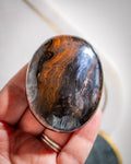 a striped brown tigers iron crystal palmstone being held on a flat palm against a white background